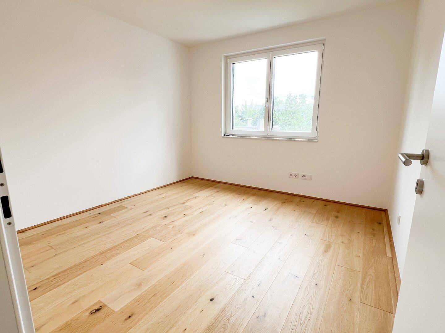 Ruhiges Zimmer mit hellem Holzfußboden und einem Fenster, ideal als Schlaf- oder Arbeitszimmer.