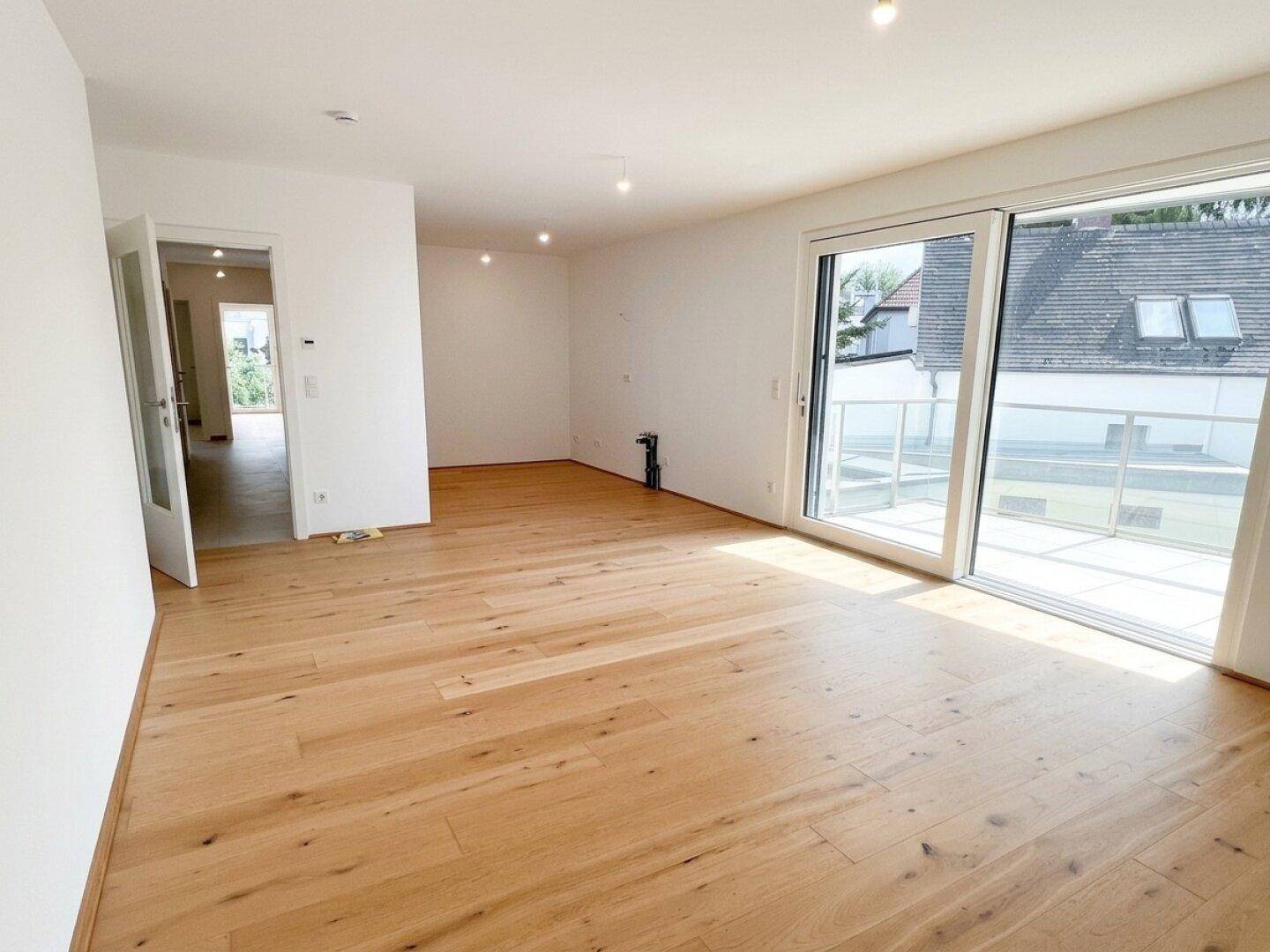 Lichtdurchfluteter Wohnbereich mit Holzboden und Zugang zu weiteren Räumen sowie zum Balkon.