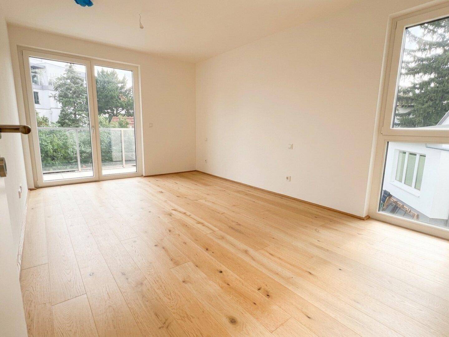 Helles Schlafzimmer mit Holzboden, großen Fenstern und direktem Zugang zum Balkon.