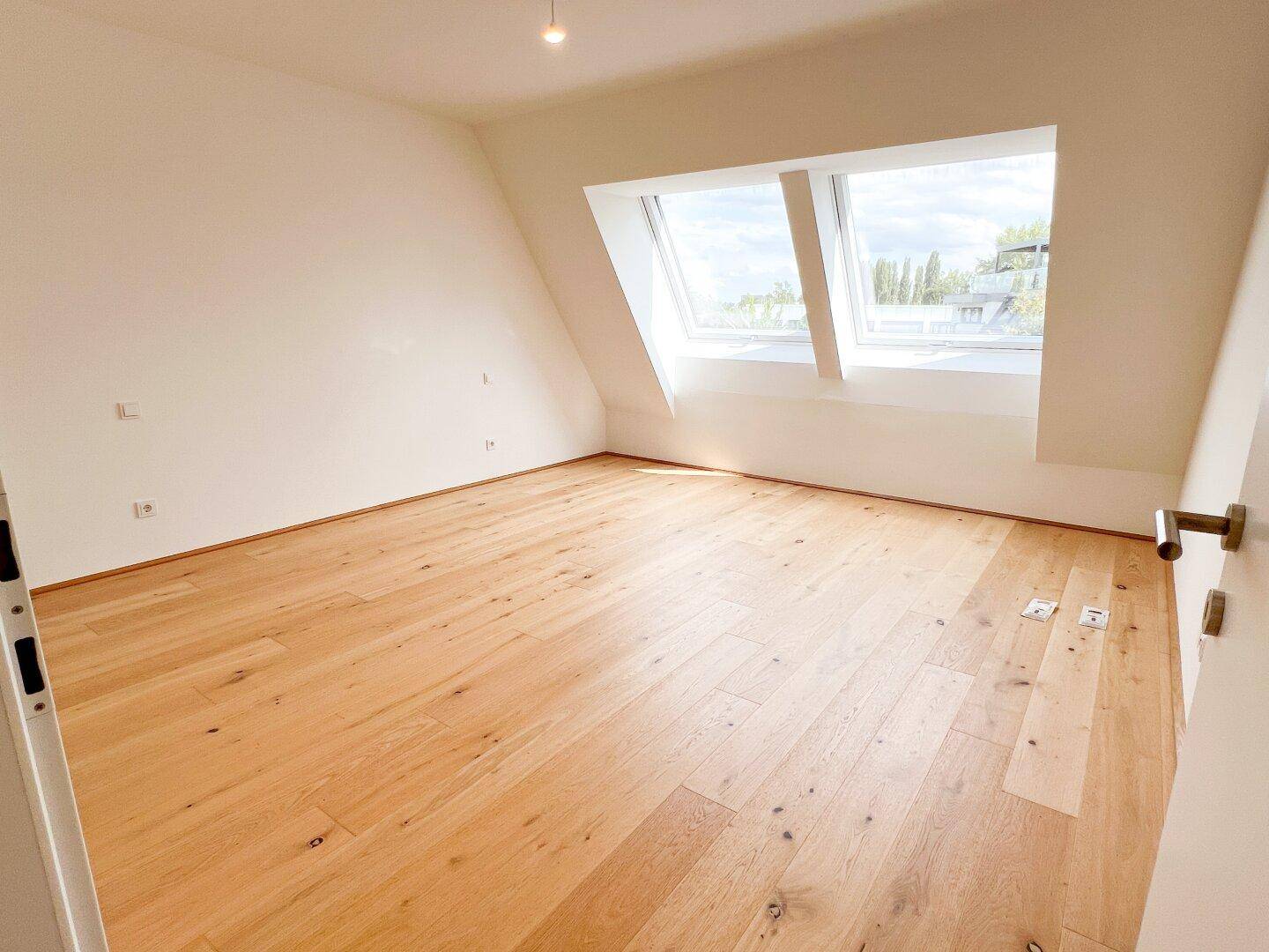 Helles Zimmer mit Holzboden und zwei großen Dachfenstern, ideal als Schlaf- oder Arbeitszimmer.