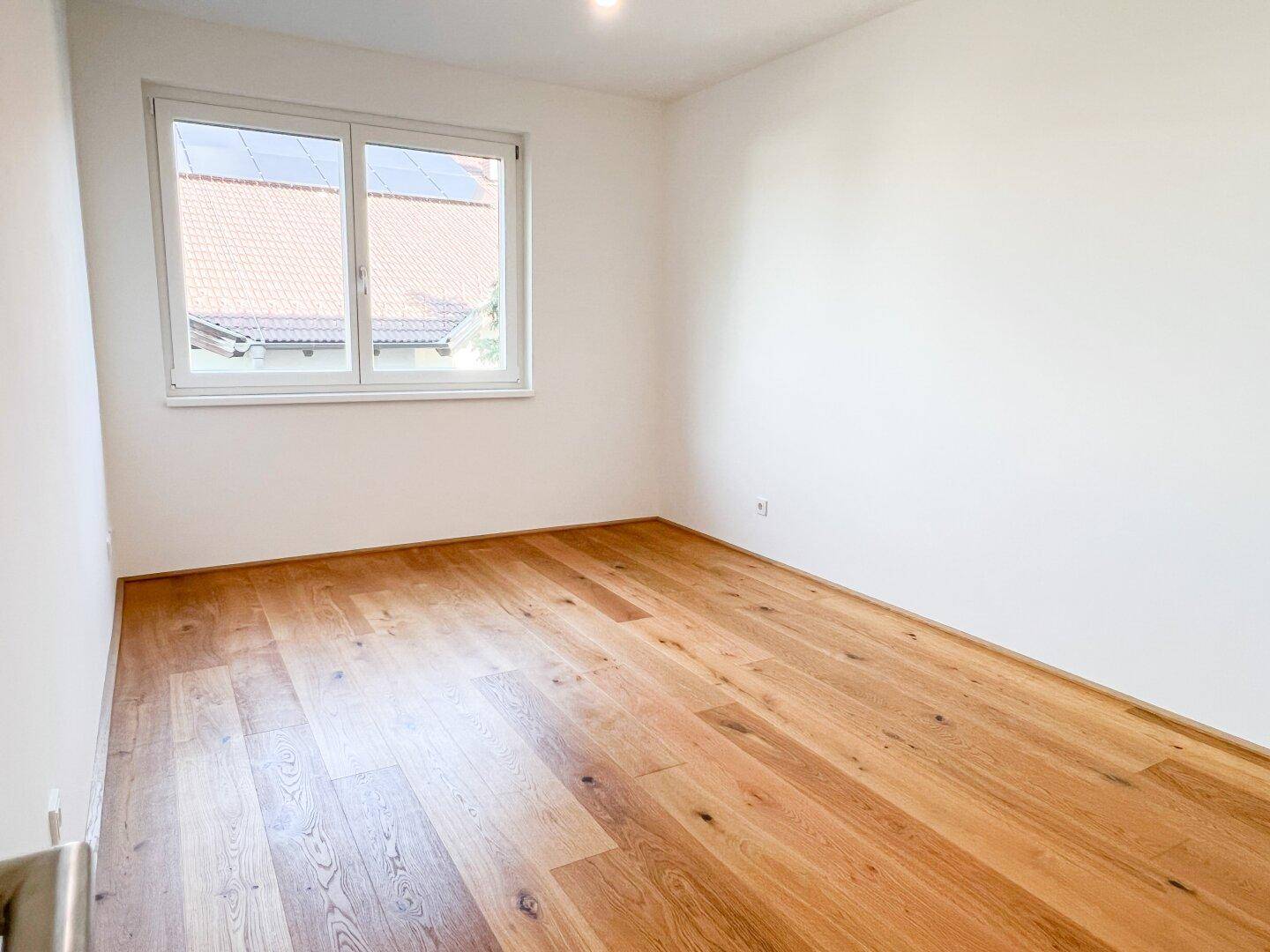 Schlafzimmer mit Holzboden und Fenster, das einen Blick auf die Dächer der Nachbarschaft bietet.