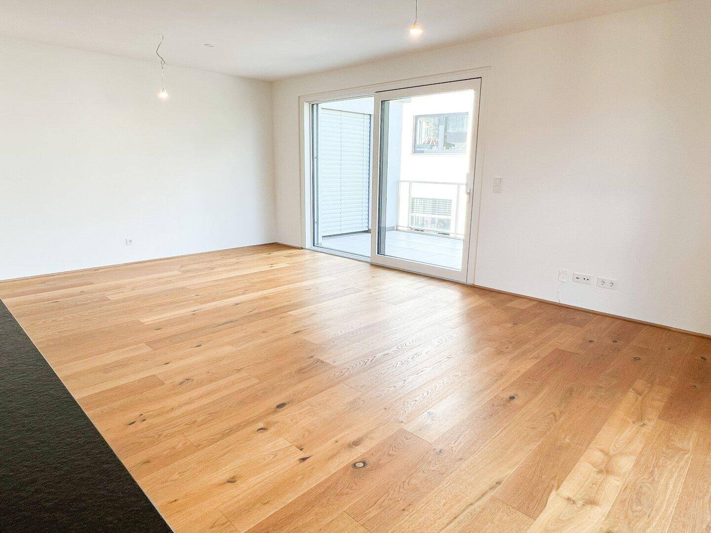 Heller Wohnbereich mit Holzboden und breiter Schiebetür, die auf einen Balkon führt.