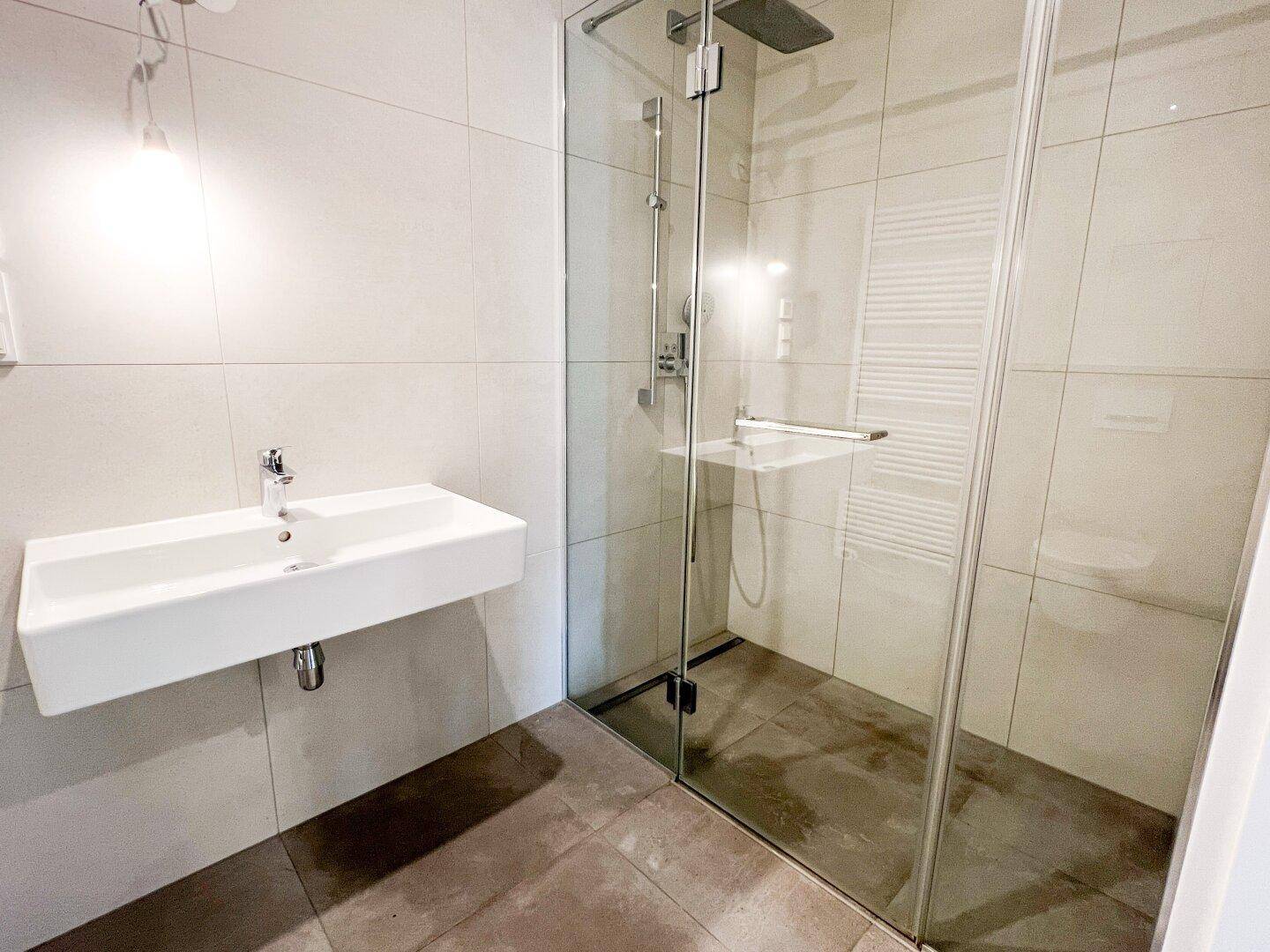 Modernes Badezimmer mit Einzelwaschbecken, begehbarer Dusche und beheiztem Handtuchhalter.