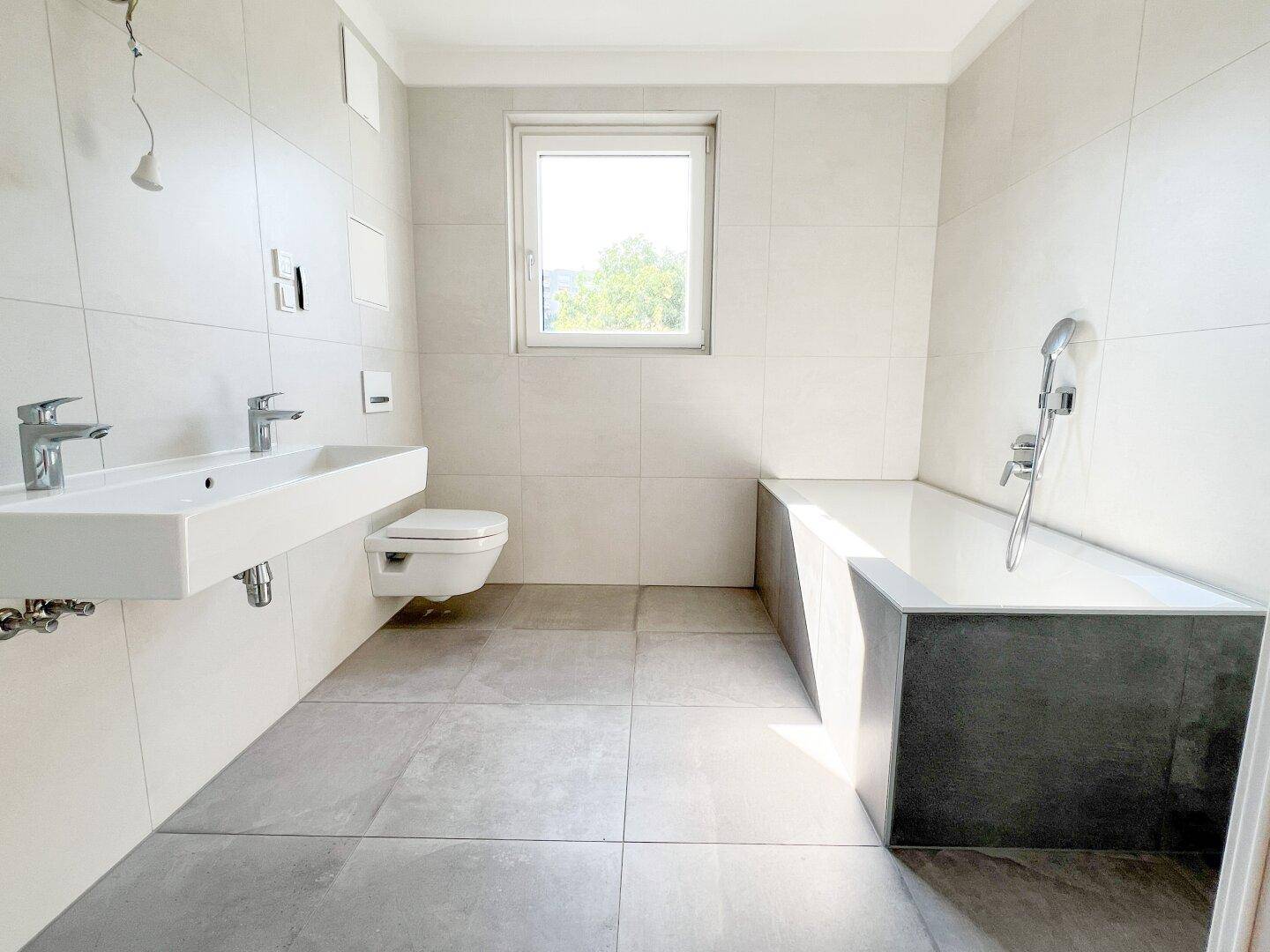 Modernes Badezimmer mit Doppelwaschbecken, Badewanne, WC und Fenster.
