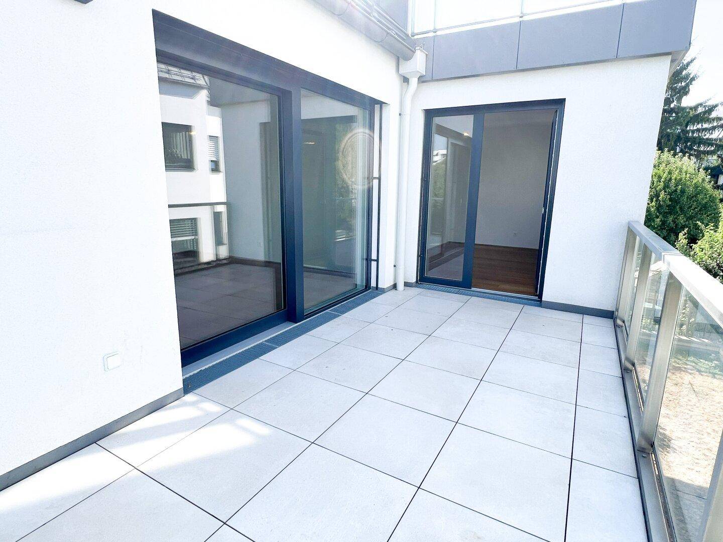 Geräumiger Balkon mit Fliesenboden und großen Glastüren, die in die Innenräume führen.