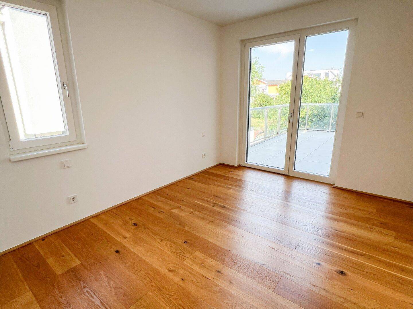 Helles Schlafzimmer mit Holzboden und Zugang zu einem Balkon durch eine Glastür.