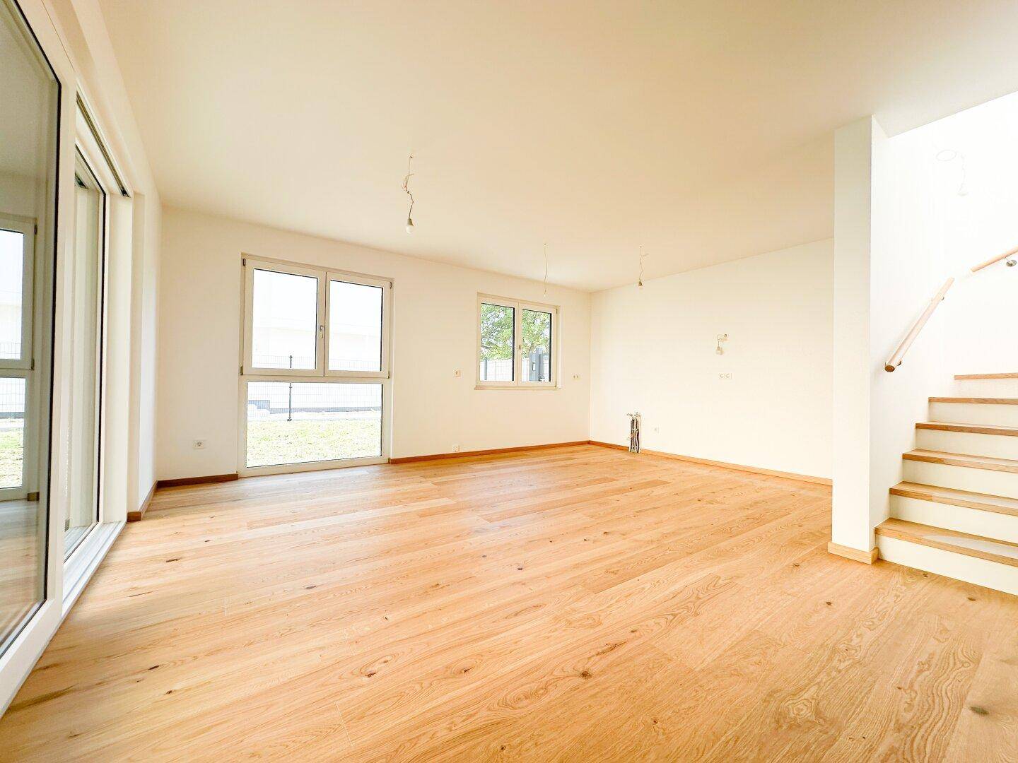 Helles, leeres Wohnzimmer mit Eichenparkettboden und großen Fenstern.