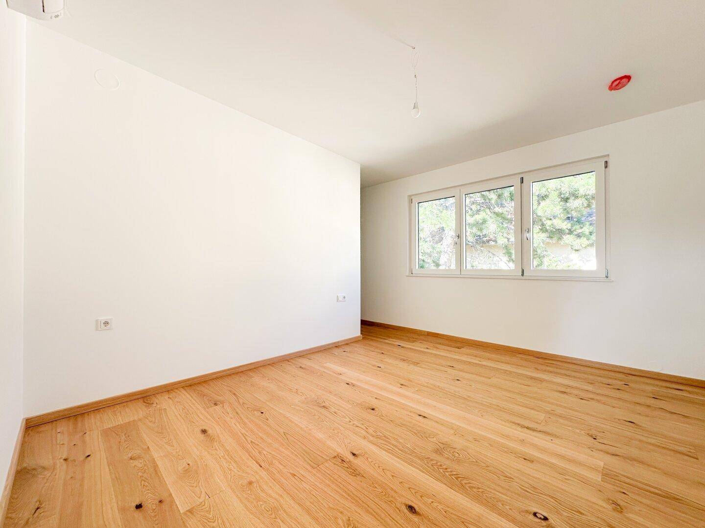 Geräumiges Schlafzimmer mit Eichenparkettboden und drei Fenstern.
