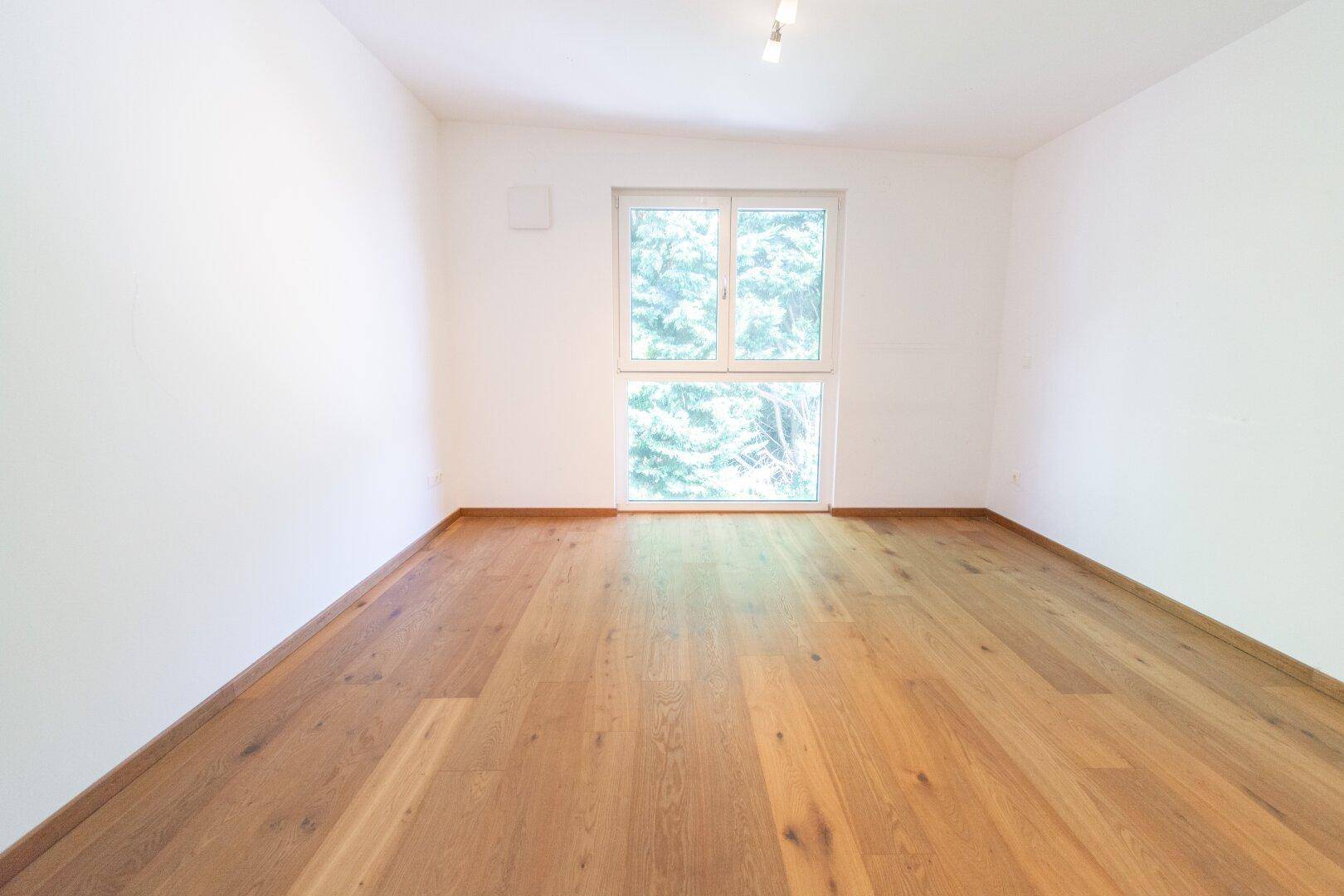 Geräumiges Schlafzimmer mit Parkettboden und viel Tageslicht durch das große Fenster.