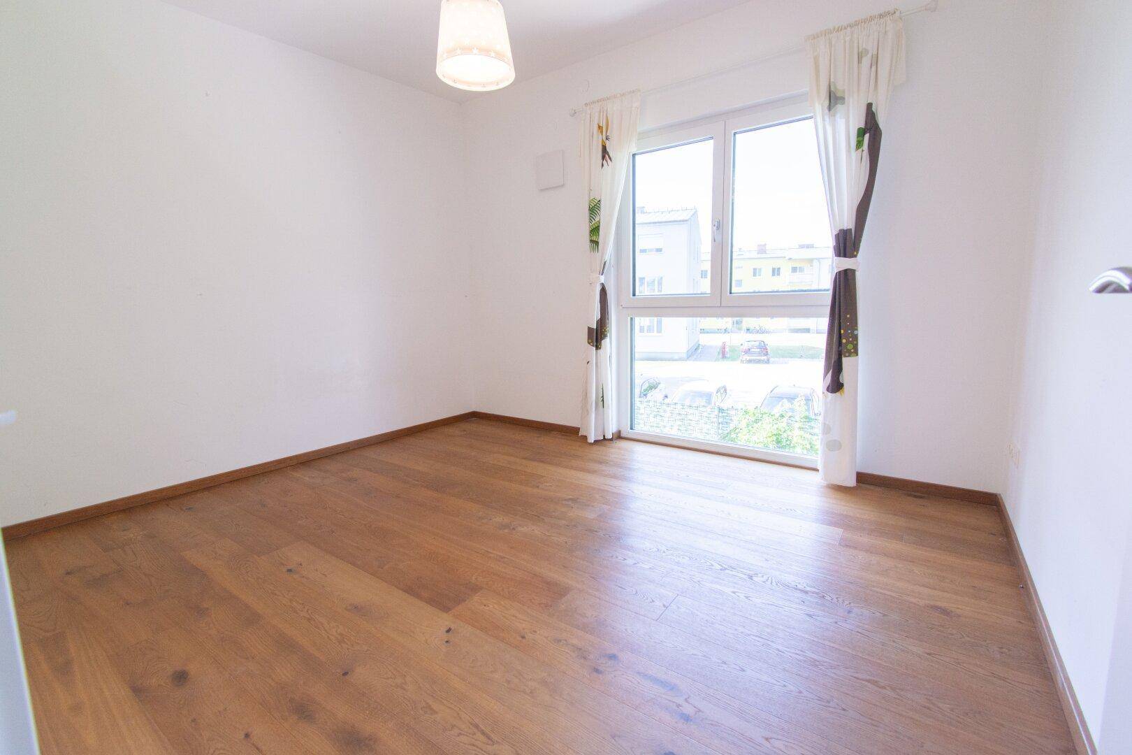 Schlafzimmer mit Holzboden und Fenster, das viel natürliches Licht hereinlässt.