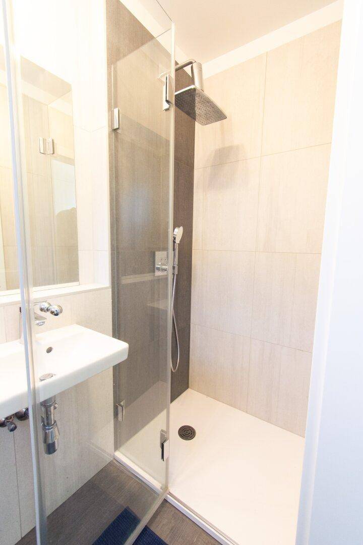 Moderne begehbare Dusche mit Regenduschkopf und eleganten Fliesen.