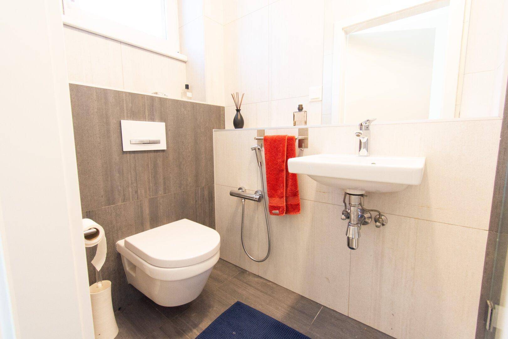 Gäste-WC mit wandhängender Toilette, kleinem Waschbecken und modernen Fliesen.