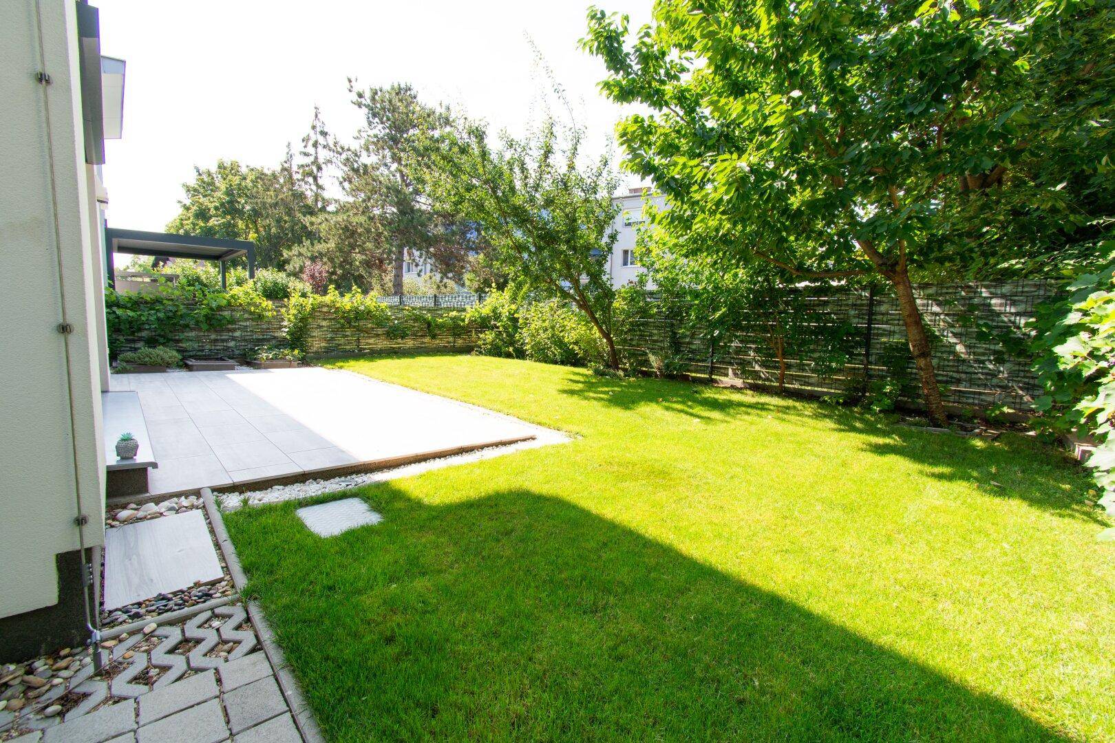 Großer, sonniger Garten mit Rasenfläche und gepflasterter Terrasse.