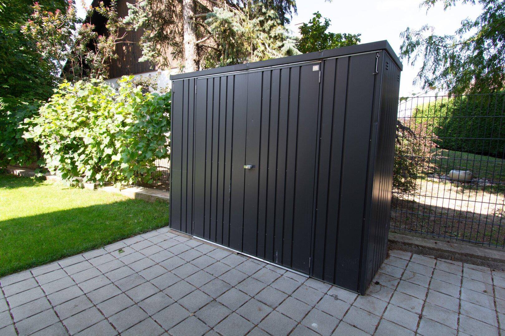 Praktischer Gartenschuppen aus Metall auf gepflastertem Untergrund im Garten.