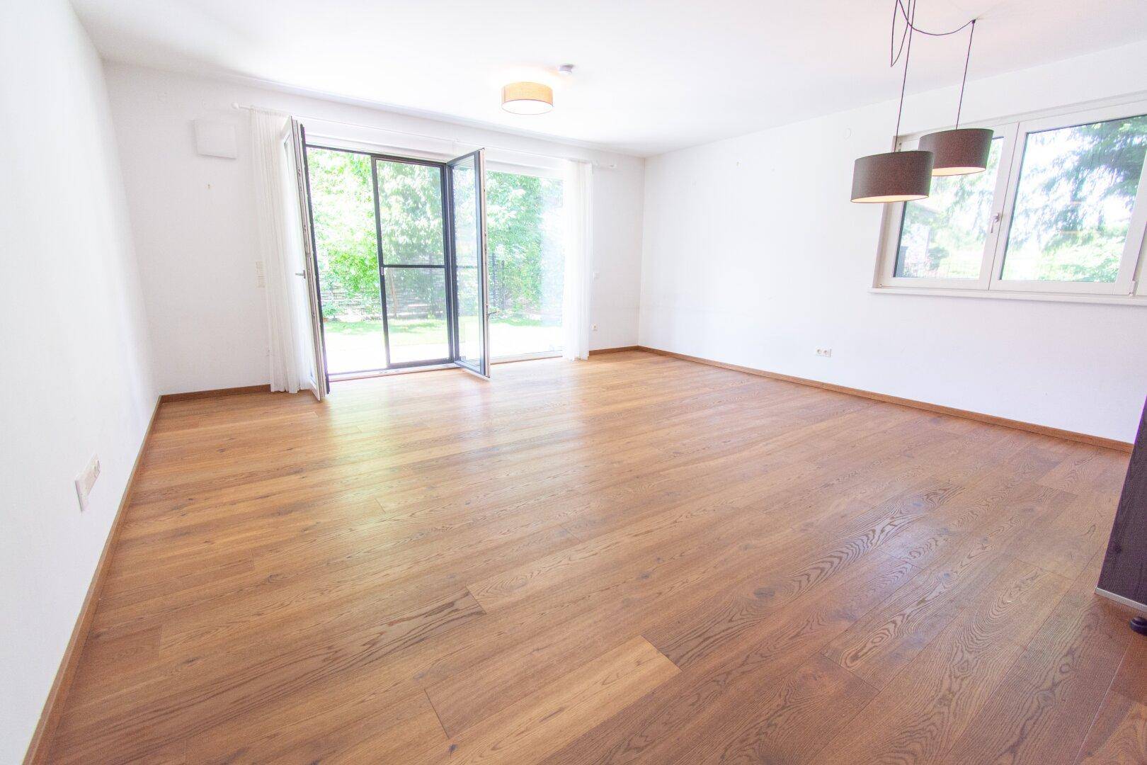 Geräumiges Wohnzimmer mit Eichenparkett und viel Tageslicht durch große Fenster.