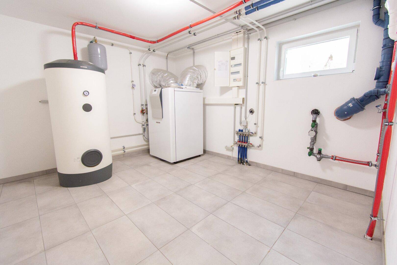 Technikraum mit Heizungsanlage, Warmwasserspeicher und sichtbaren Installationen.