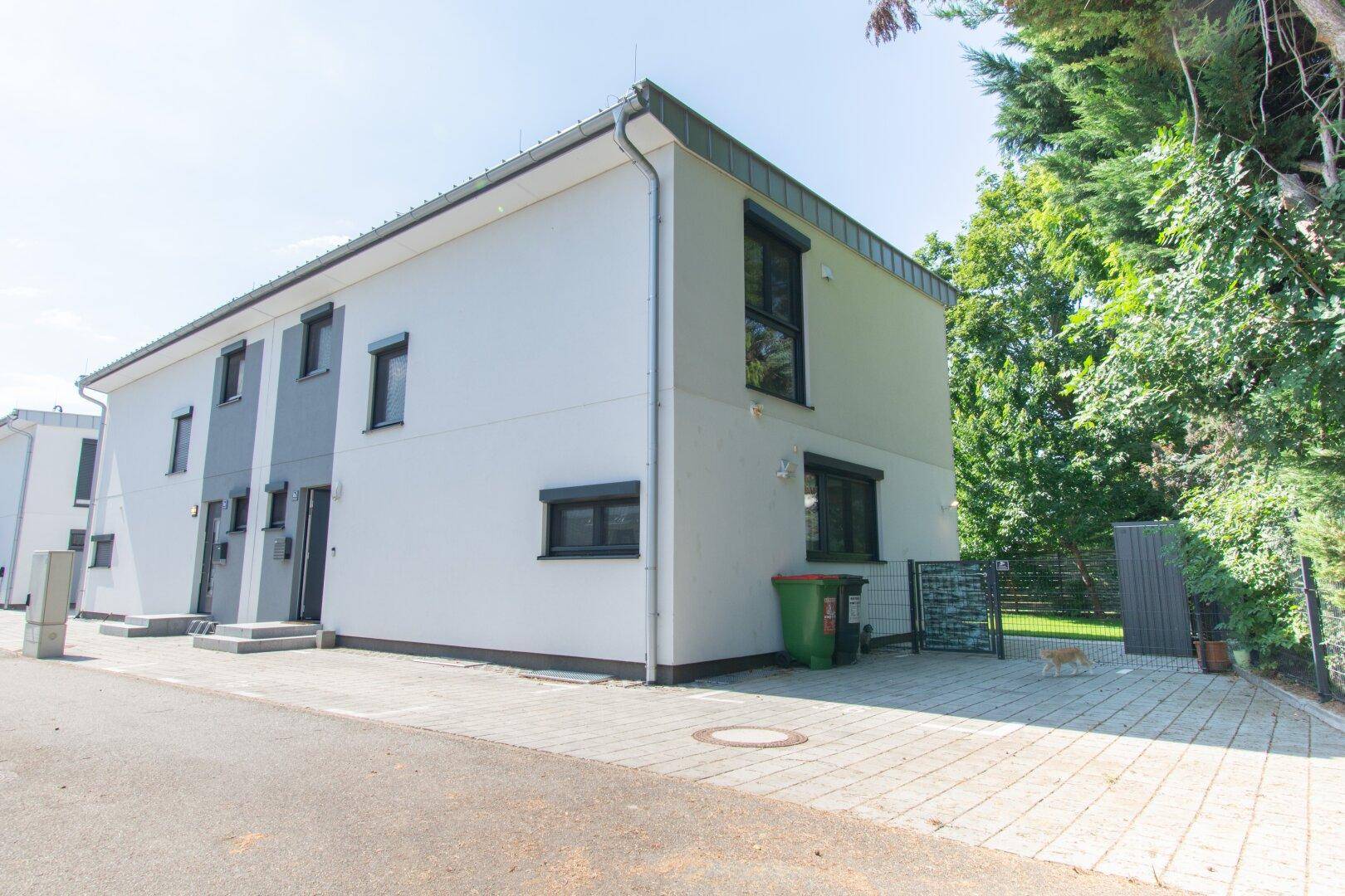 Moderne Reihenhausfassade mit grau-weißer Farbgebung und gepflasterter Zufahrt.