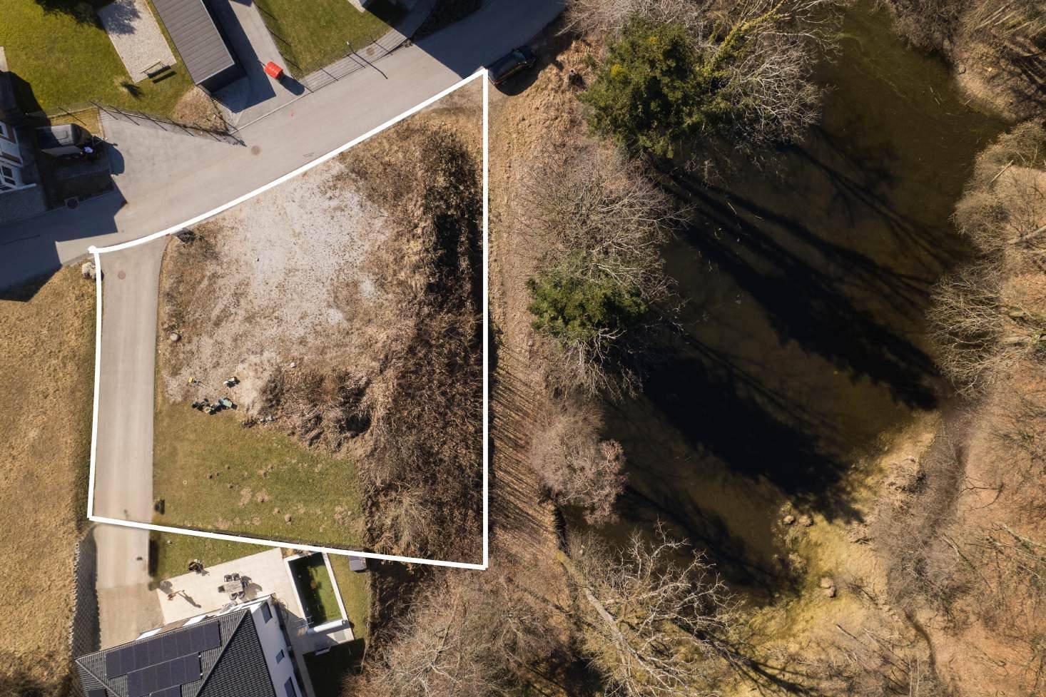 Luftaufnahme eines unbebauten Grundstücks, umgeben von Natur und angrenzend an eine Straße.