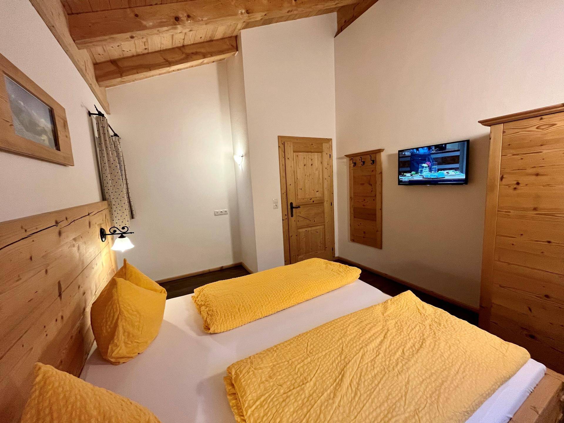 Detailansicht eines Schlafzimmers mit Holzvertäfelung, Holzbalkendecke und Fernseher.