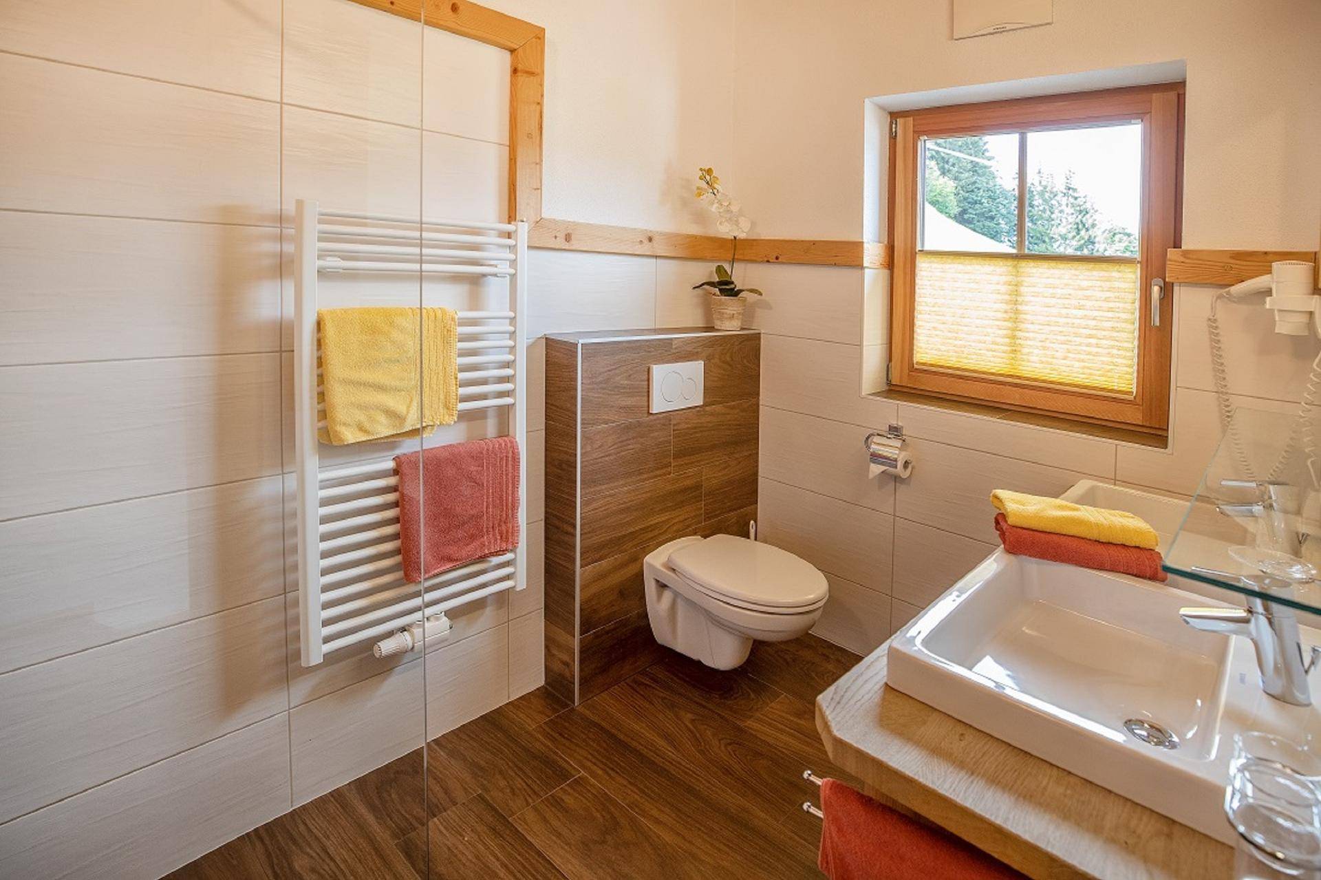 Modernes Badezimmer mit Holzboden, weißen Fliesen, wandhängendem WC und Handtuchheizkörper.