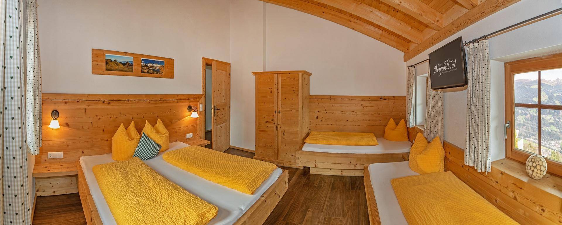 Gemütliches Schlafzimmer im alpinen Stil mit mehreren Betten, Holzvertäfelung und Bergblick.