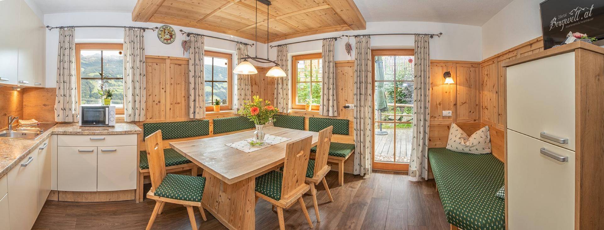 Gemütliche Wohnküche im alpinen Stil mit Holztisch, Eckbank und Zugang zum Garten.