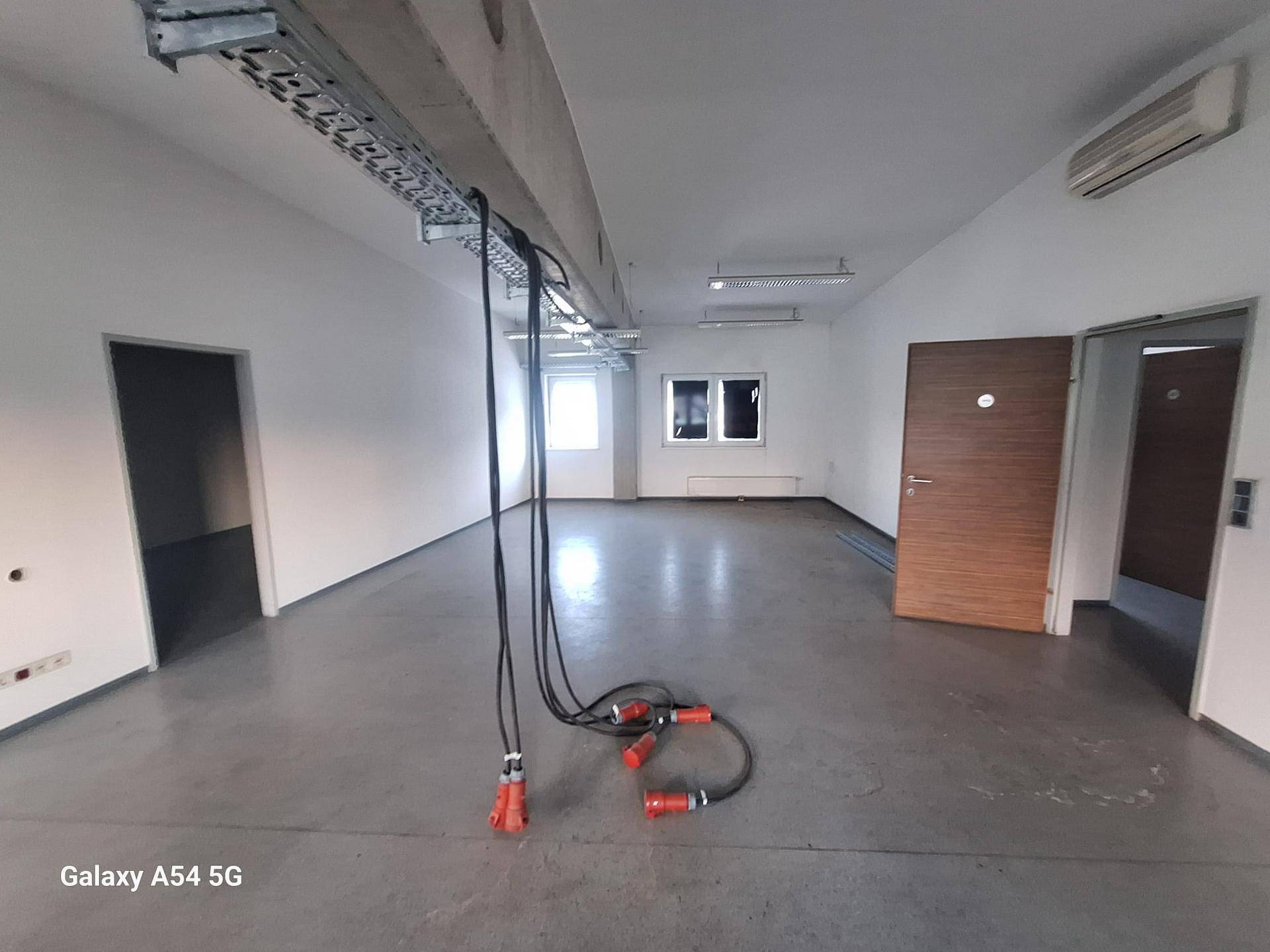 Heller Büroraum mit Betonboden, Klimaanlage, sichtbaren Kabelkanälen und großen Fenstern.