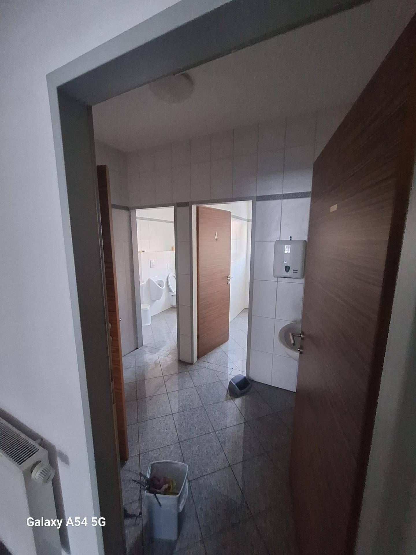 Eingangsbereich zu einem Badezimmer mit gefliestem Boden, Waschbecken und Blick auf weitere Sanitäranlagen.