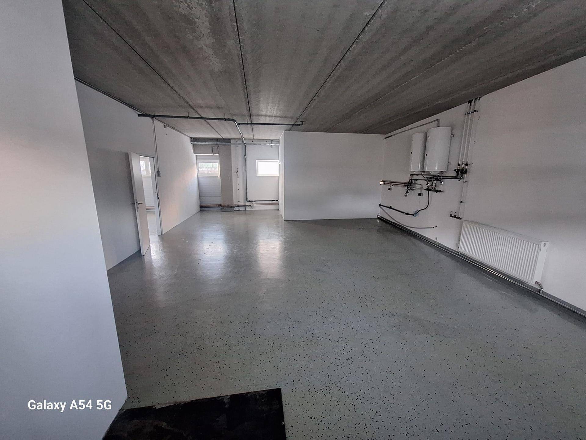 Geräumiger Versorgungsraum mit Betonboden, Heizkörpern und einem Fenster, das für Tageslicht sorgt.