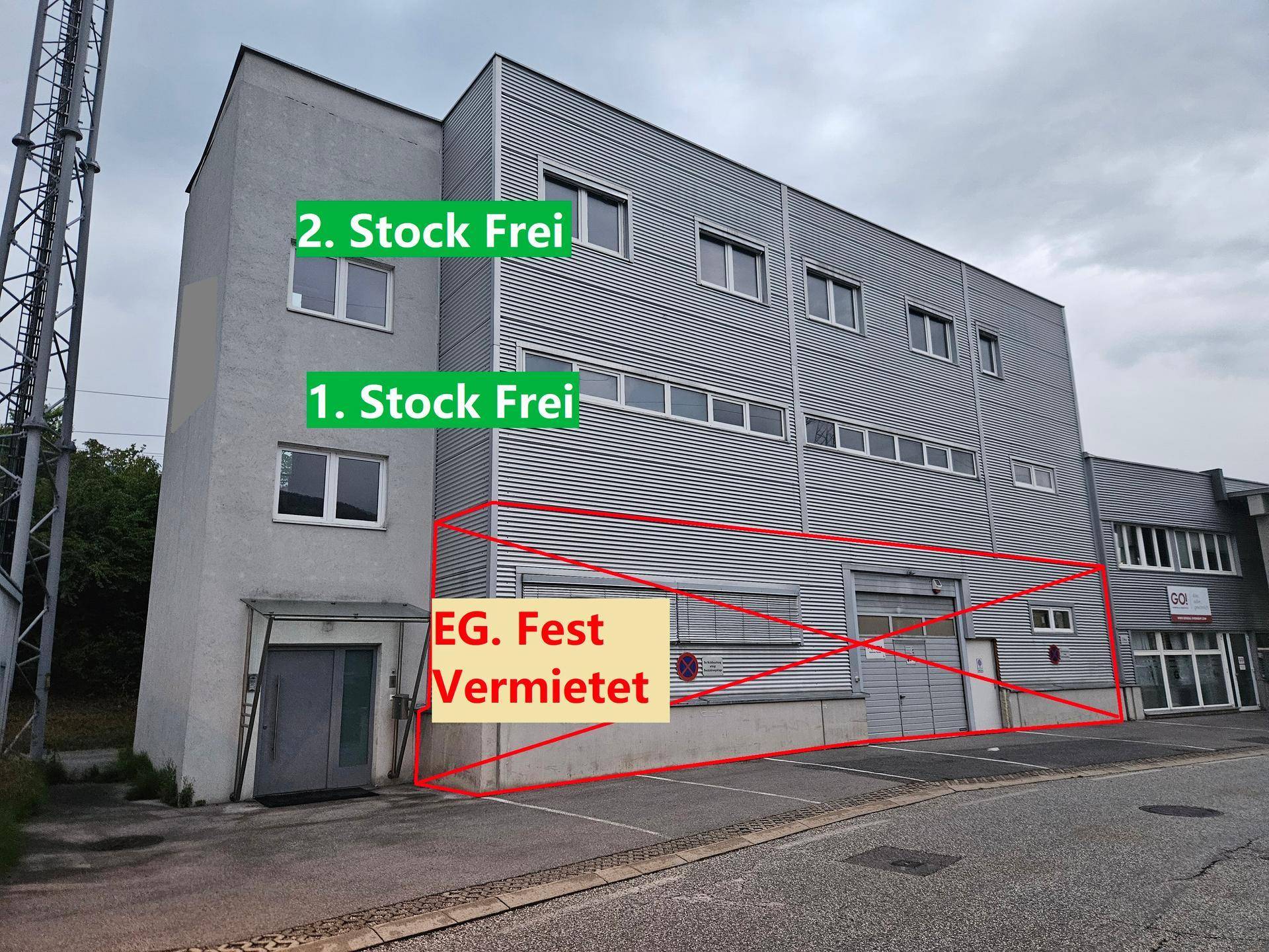 Ansicht eines grauen Gewerbegebäudes mit Stockwerksangaben und einem großen Rolltor im Erdgeschoss.