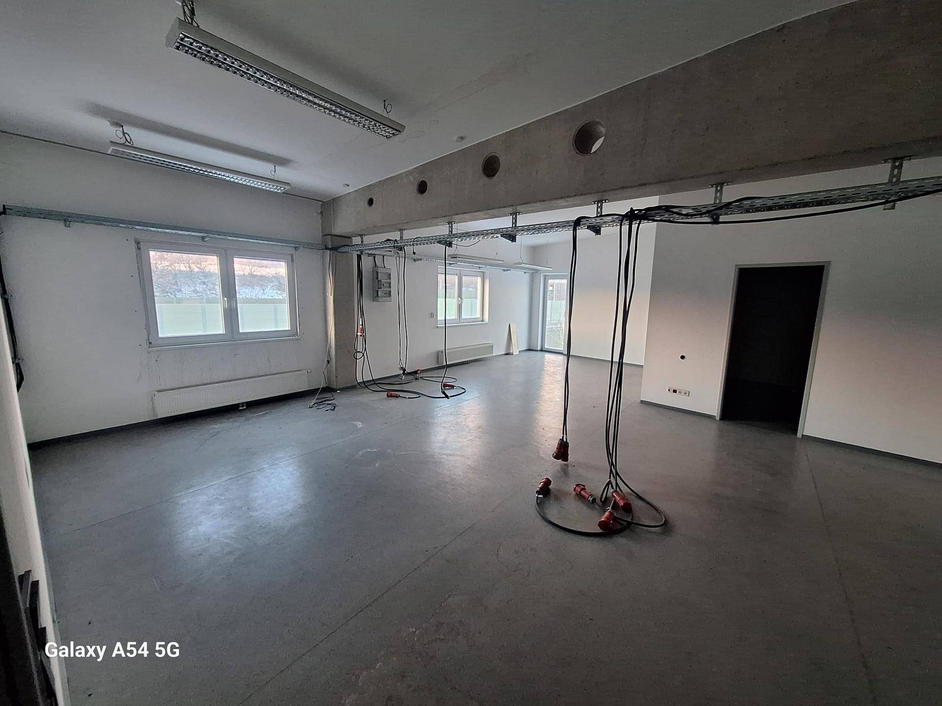 Großer Büroraum mit Betonboden, weißen Wänden, sichtbaren Installationen und Fenstern mit Ausblick.