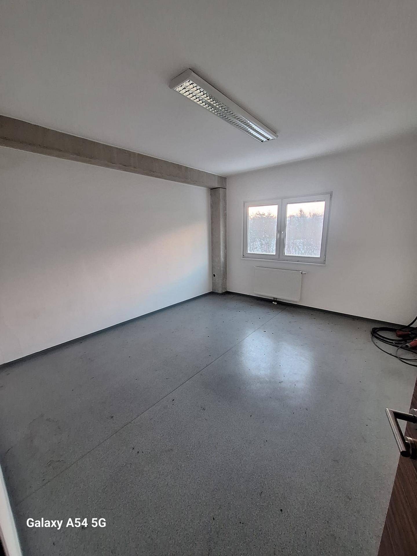 Schlichter Büroraum mit Betonboden, weißen Wänden und einem Fenster, das für natürliches Licht sorgt.