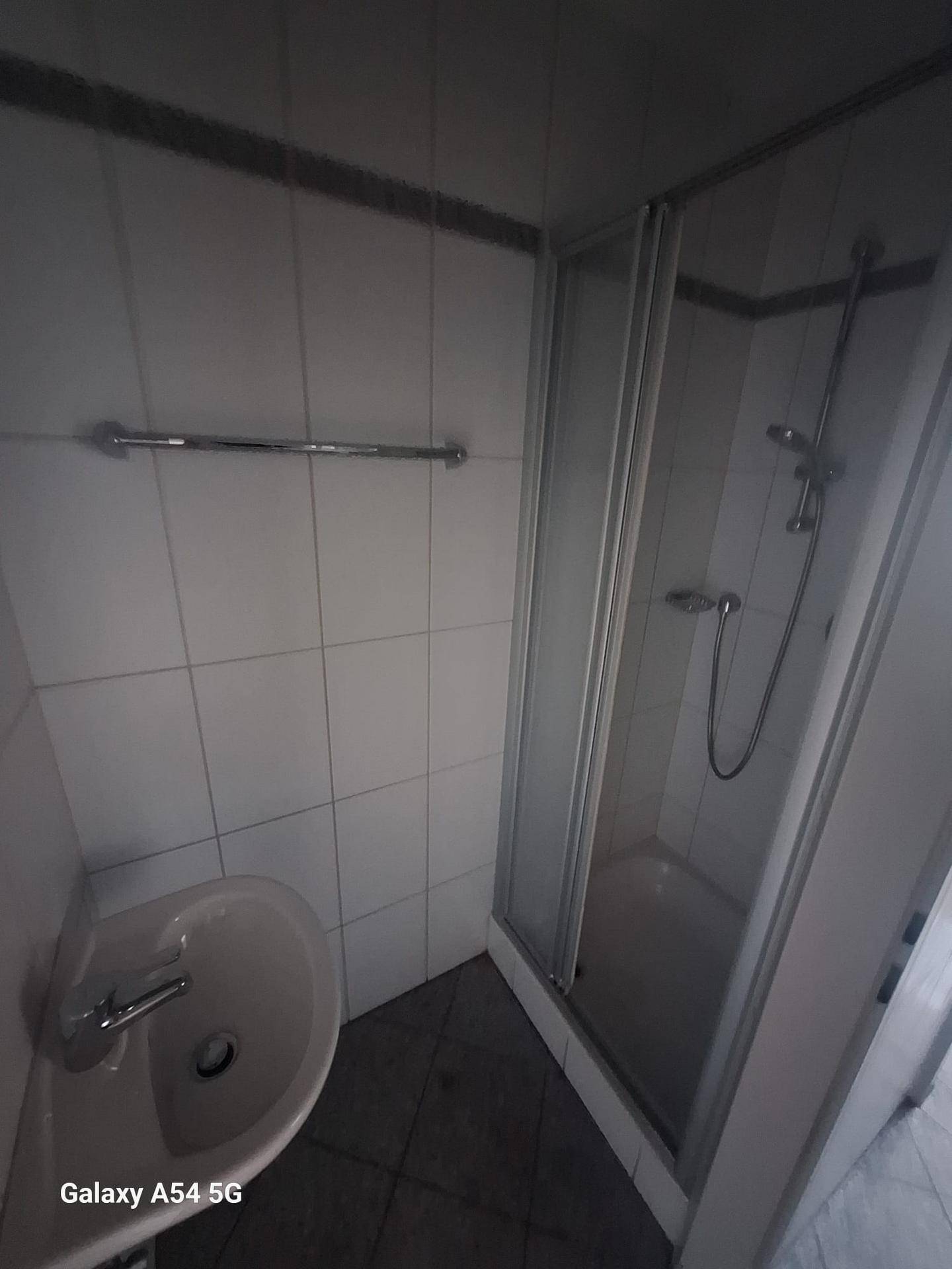 Kleines Badezimmer mit Duschkabine, Waschbecken und weißen Fliesen an den Wänden.