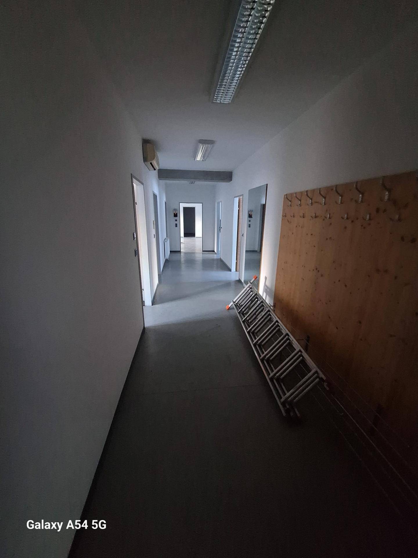 Langer Flur mit mehreren Türen, Betonboden und Deckenbeleuchtung, der zu verschiedenen Räumen führt.