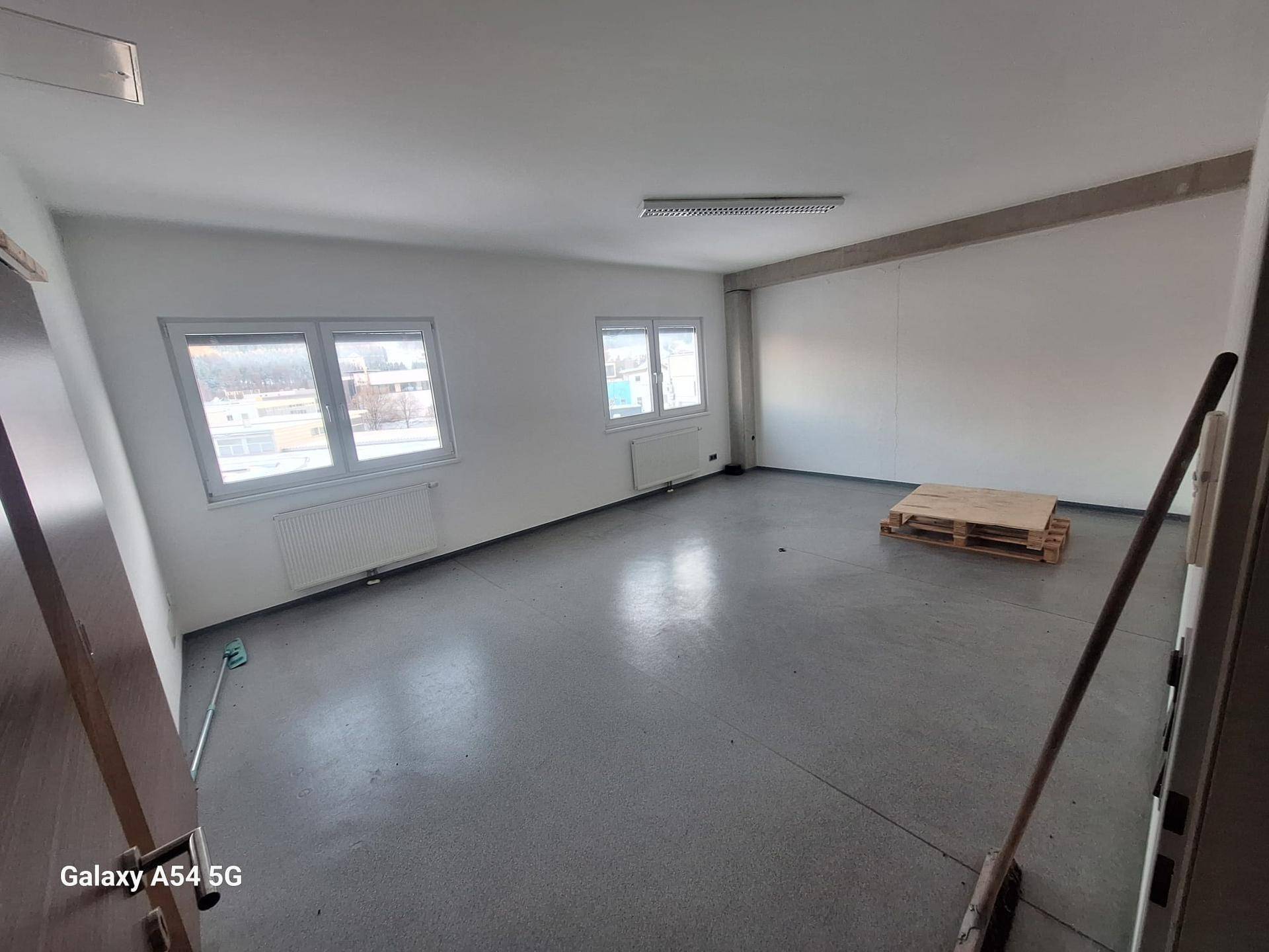 Geräumiger, leerer Büroraum mit Betonboden, weißen Wänden und mehreren Fenstern für viel Tageslicht.
