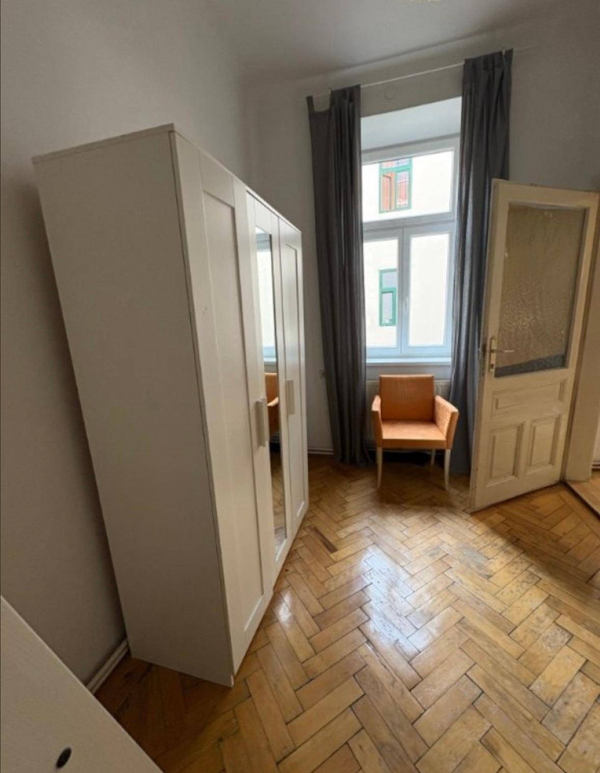 Schlafzimmer mit großem Kleiderschrank, Fenster und einem bequemen Sessel.