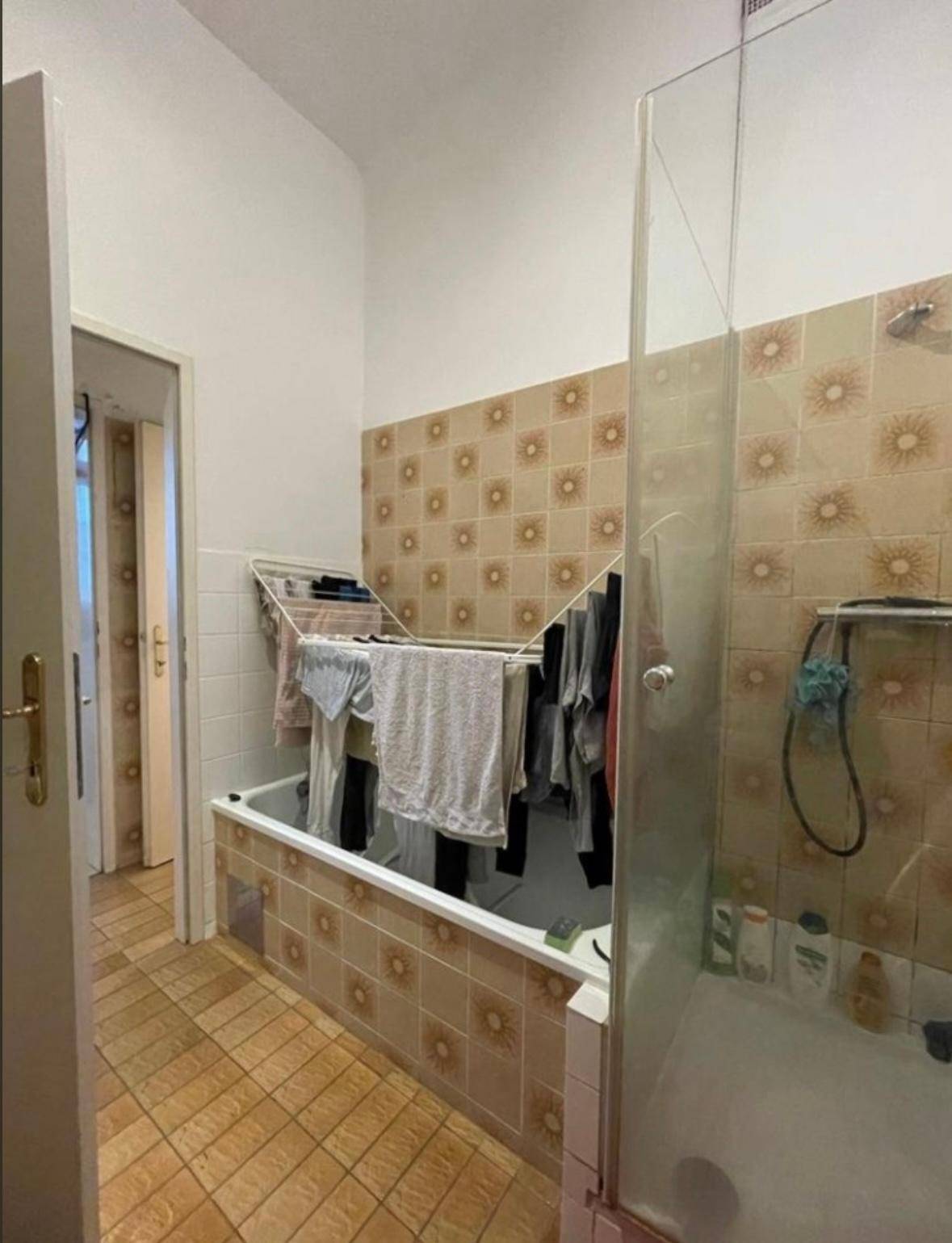 Badezimmer mit Badewanne, Duschbereich und Fliesen im 80er-Jahre-Stil.