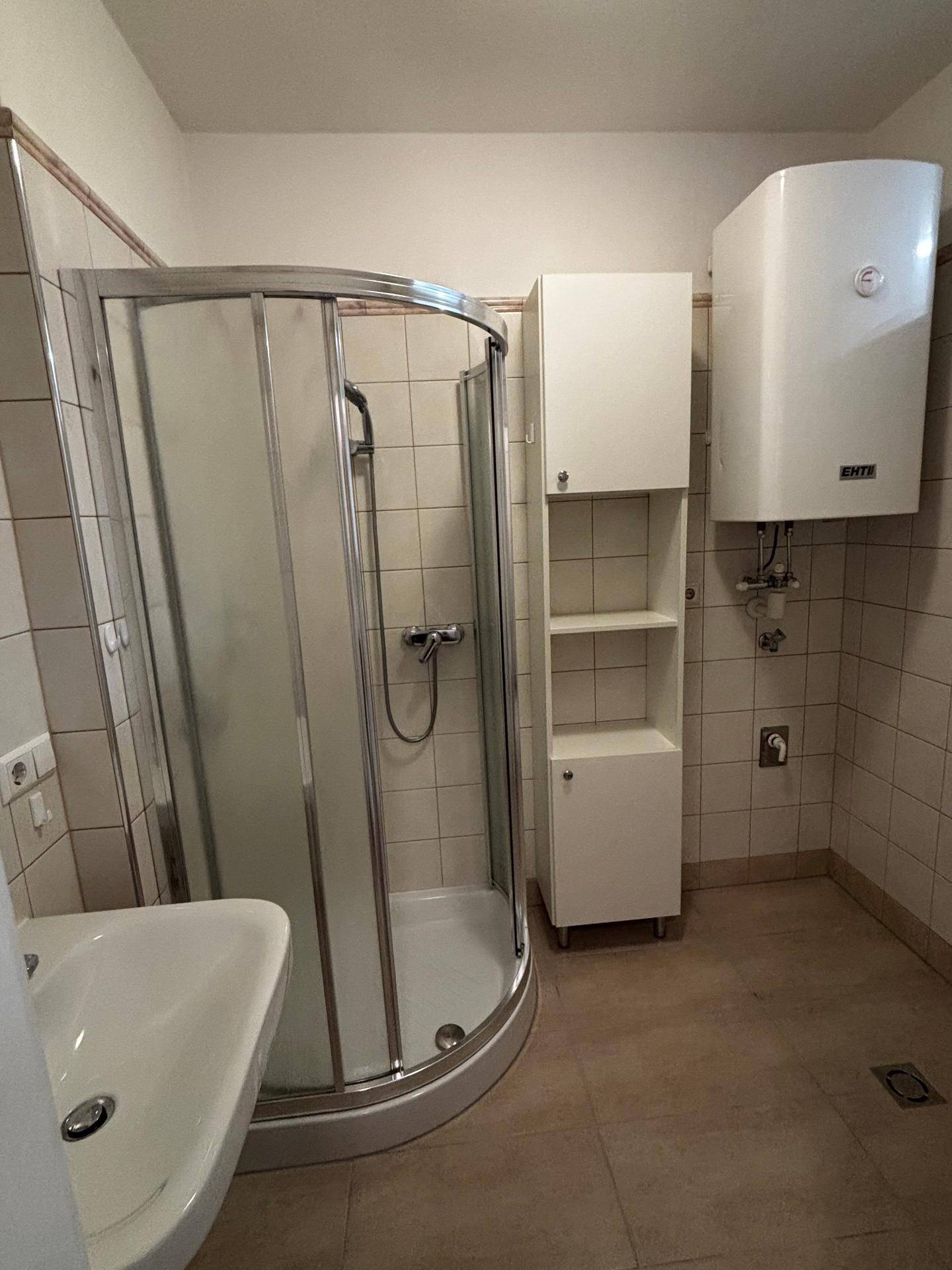 Badezimmer mit Duschkabine, Waschbecken und Boiler, funktional und hell gefliest.