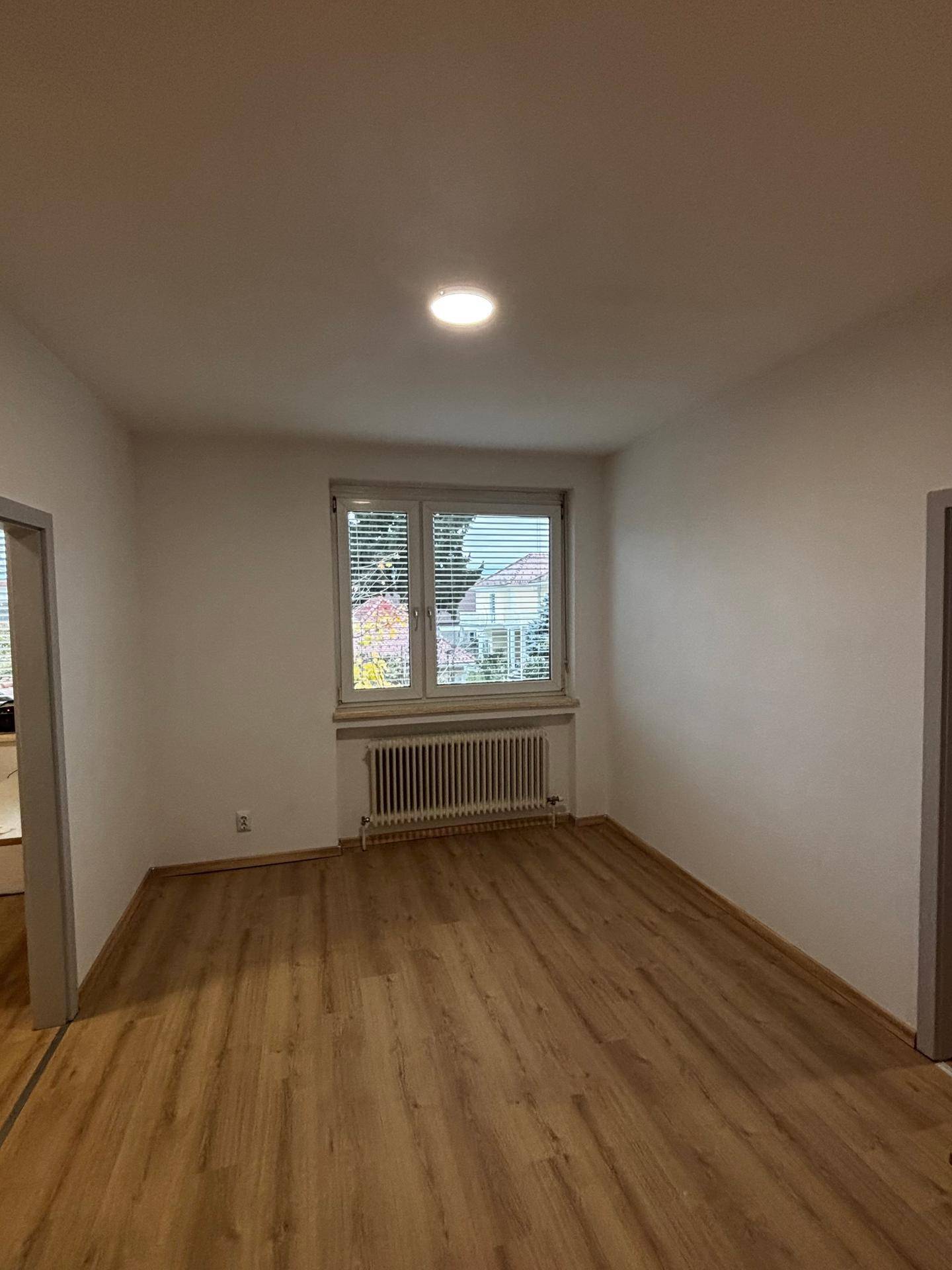 Helles, leeres Zimmer mit Laminatboden und Fenster, bereit zur individuellen Gestaltung.