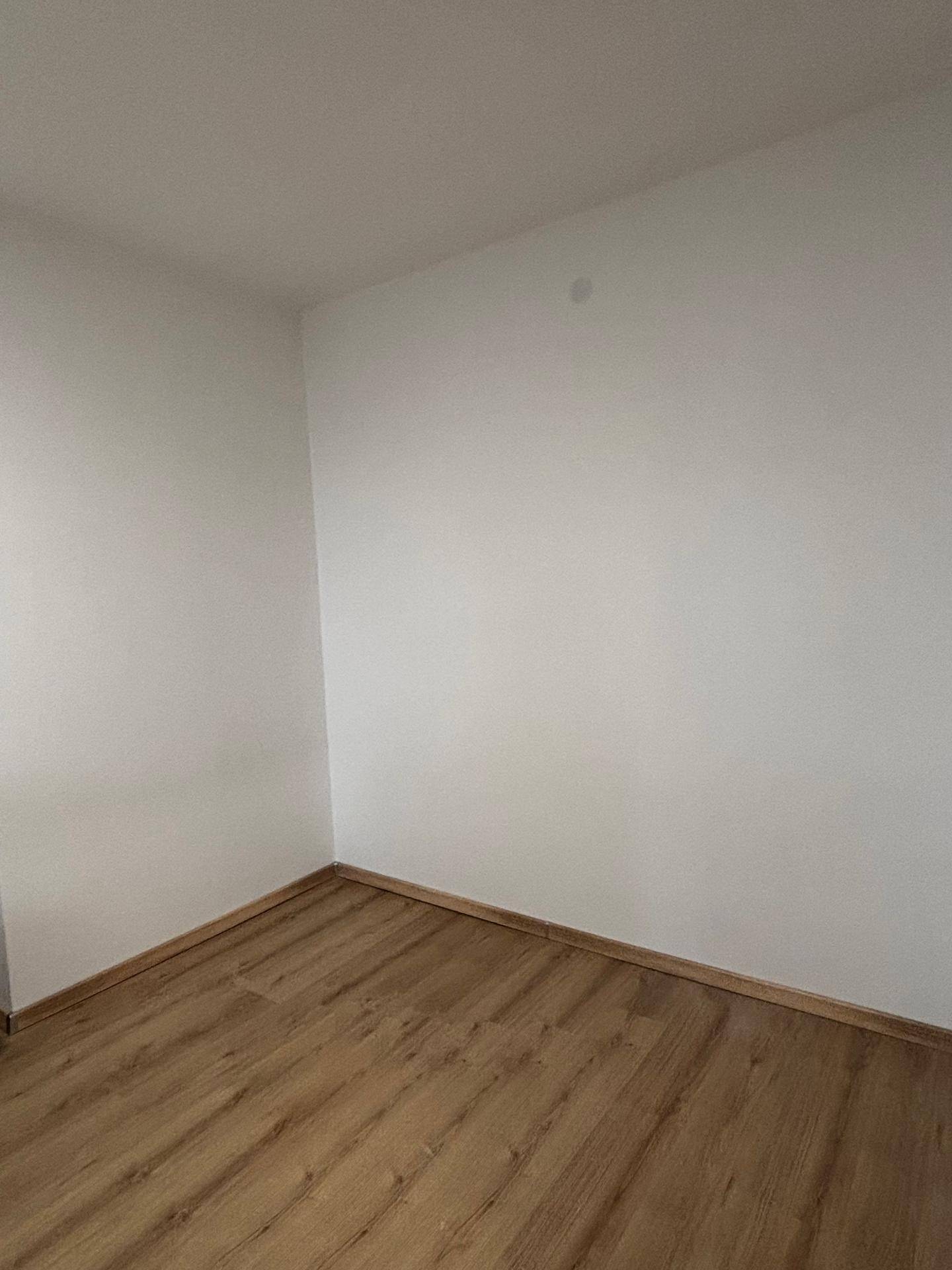 Leerer Raum mit Laminatboden und weißen Wänden, der vielseitig nutzbar ist.