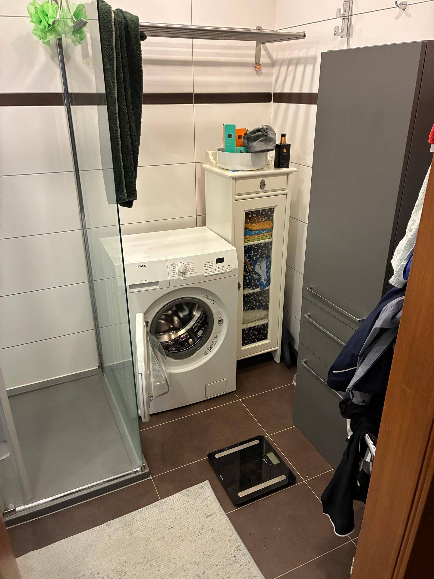 Funktionales Badezimmer mit Waschmaschine, Duschkabine und praktischen Aufbewahrungsmöbeln.
