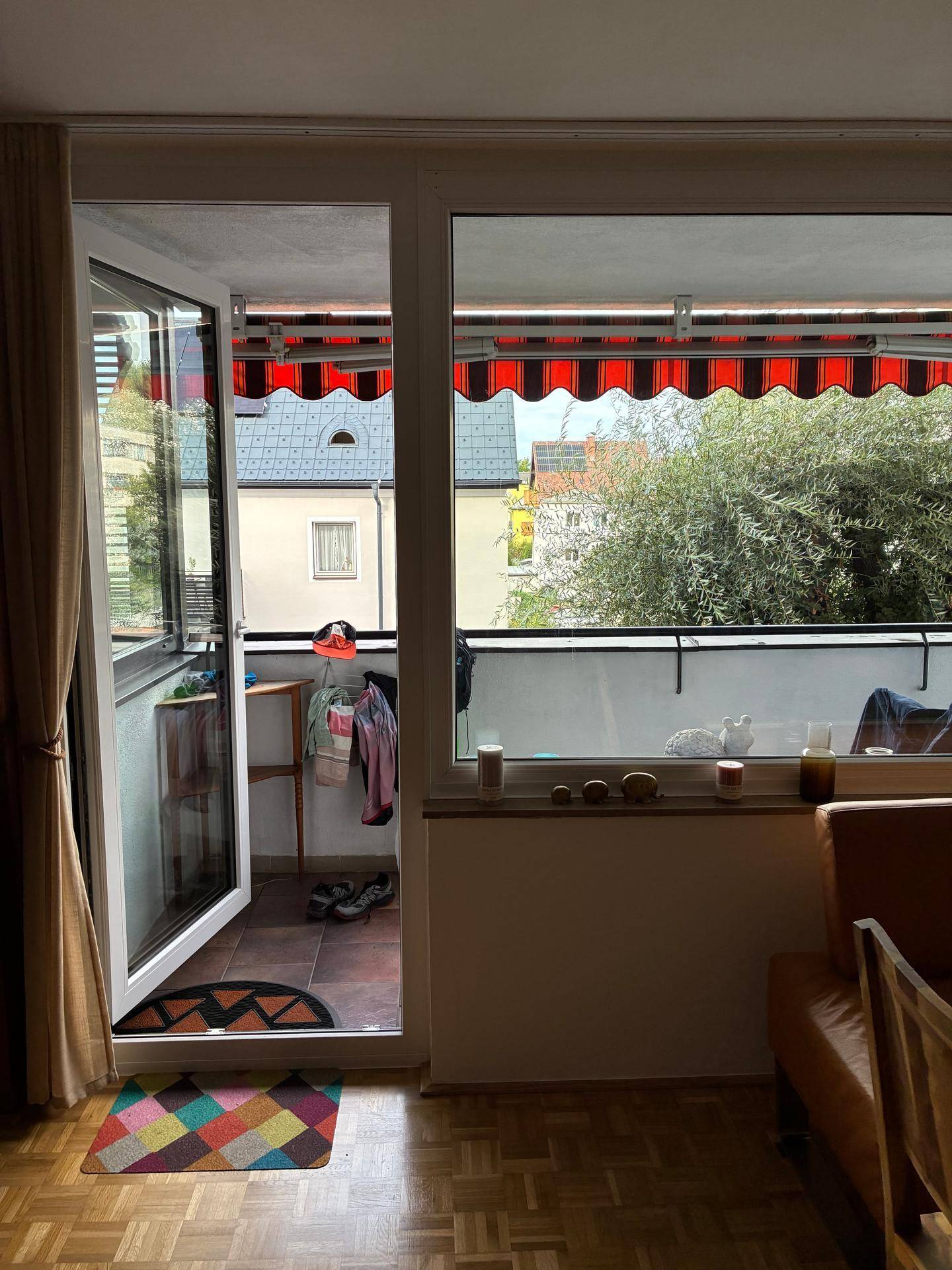 Heller Wohnbereich mit Zugang zum Balkon, der mit einer roten Markise ausgestattet ist.