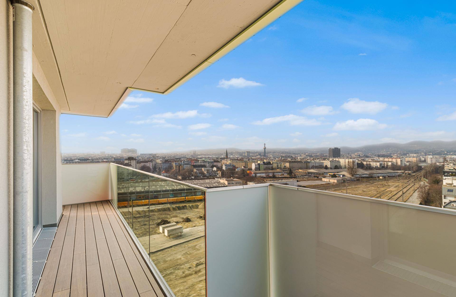 Geräumiger Balkon mit Holzboden und Glasgeländer bietet weiten Blick über die Stadt und Berge.