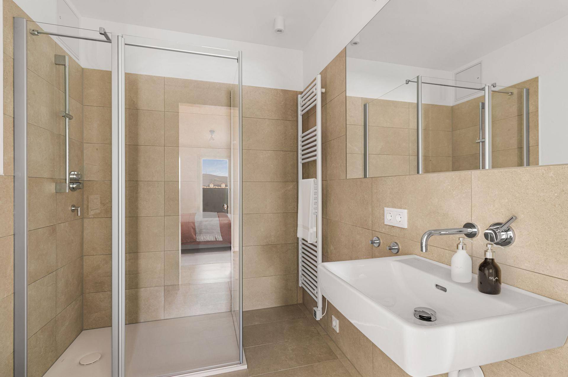 Modernes Badezimmer mit beigefarbenen Fliesen, ebenerdiger Dusche und großem Spiegel.