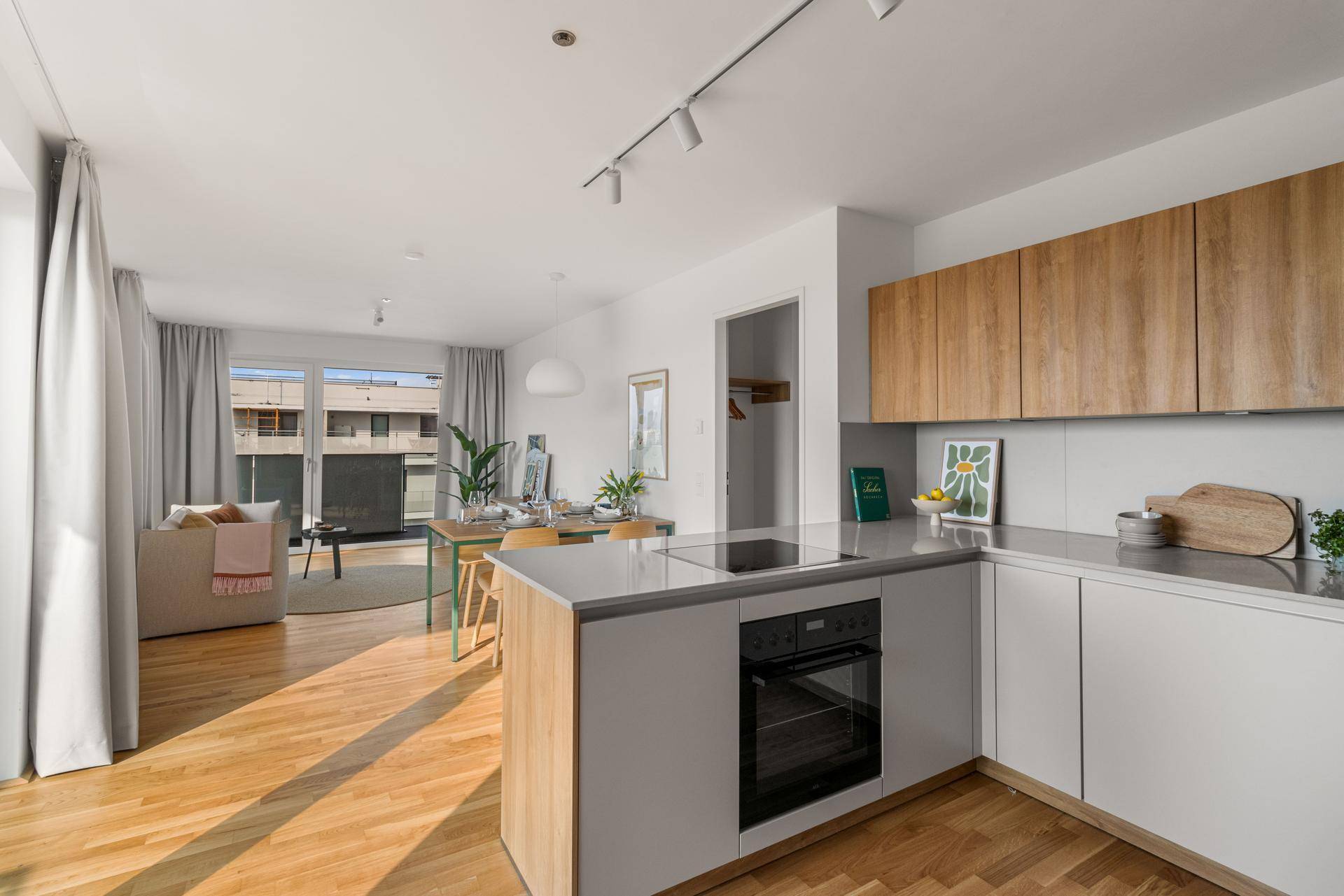 Heller offener Wohnbereich mit moderner Küche, Essbereich und Zugang zum Balkon.