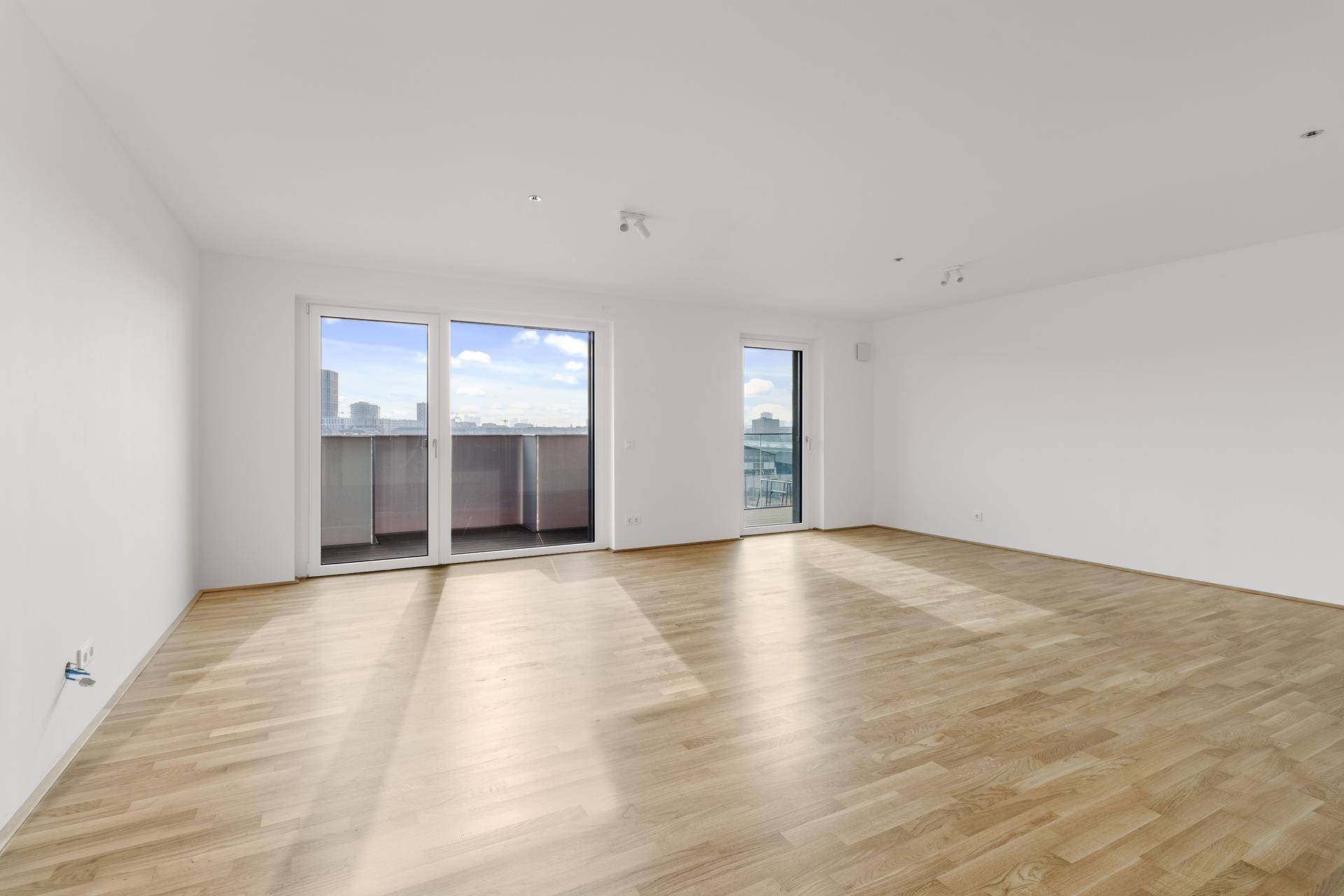 Weitläufiger Wohnraum mit Parkettboden und großen Fenstern, die einen Panoramablick über die Stadt bieten.
