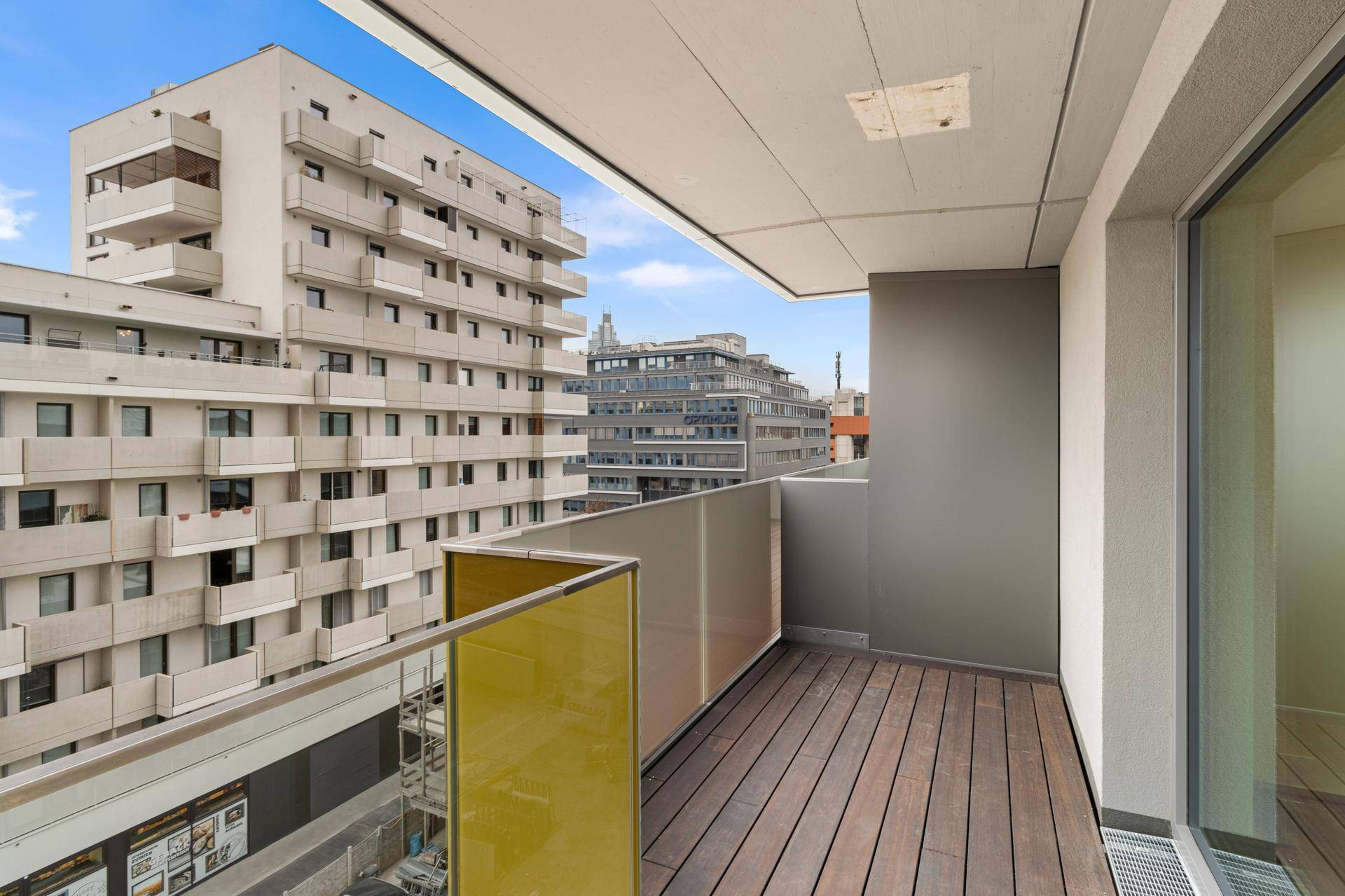 Moderner Balkon mit Holzboden und Glasgeländer, bietet einen weiten Blick auf die umliegende Stadtbebauung.