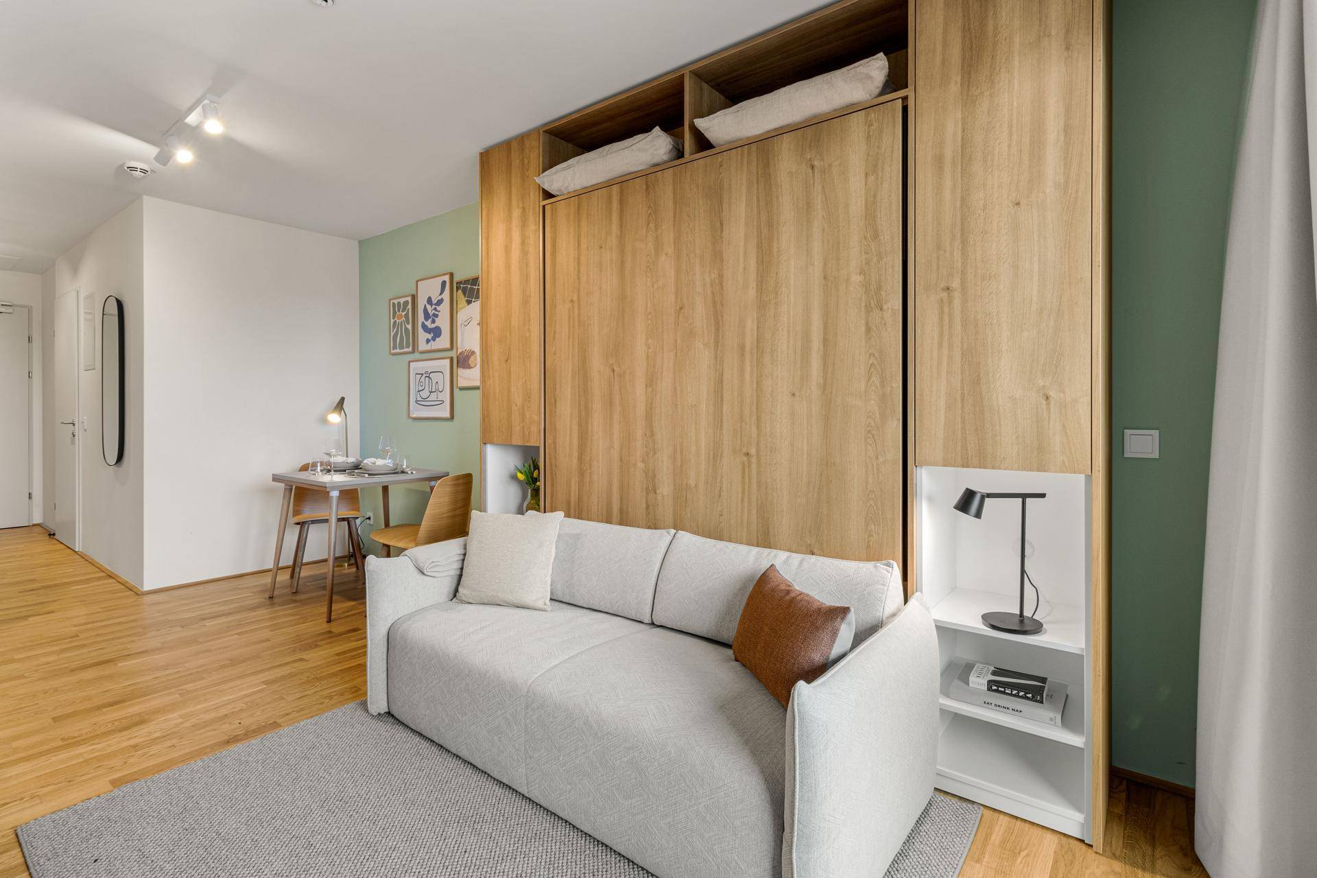 Geräumiger Wohnbereich mit Schlafsofa, Schreibtisch und moderner Dekoration an der grünen Wand.