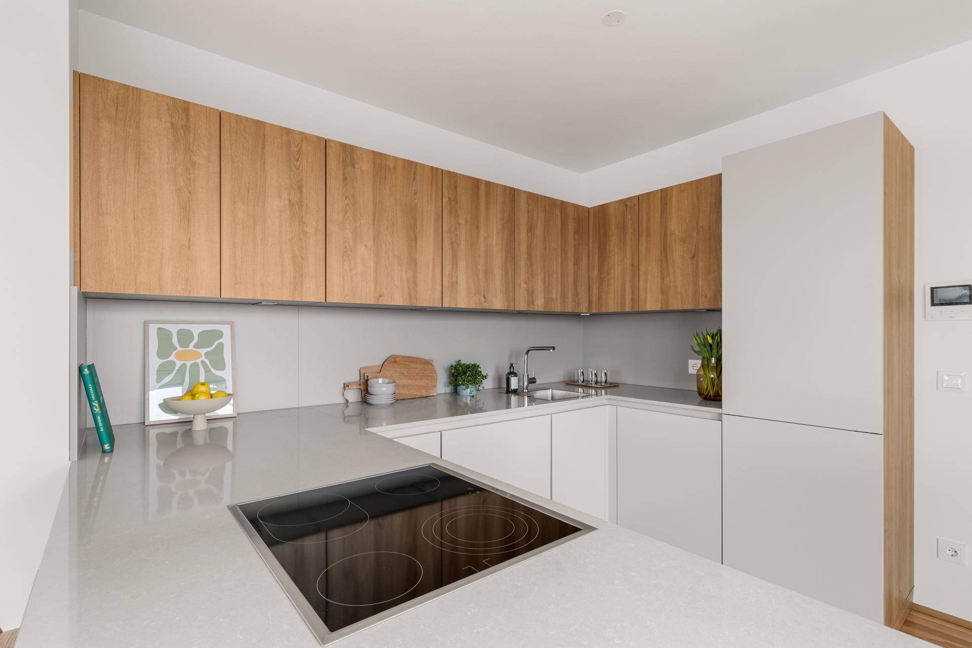 Moderne Küche mit Holz- und weißen Schränken, Induktionskochfeld und heller Arbeitsplatte.