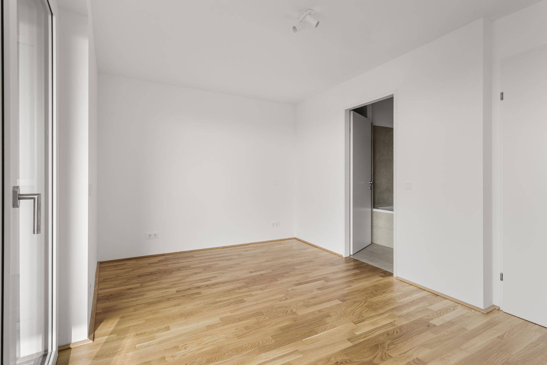 Helles Schlafzimmer mit Parkettboden und Zugang zu einem modernen Badezimmer mit Badewanne.